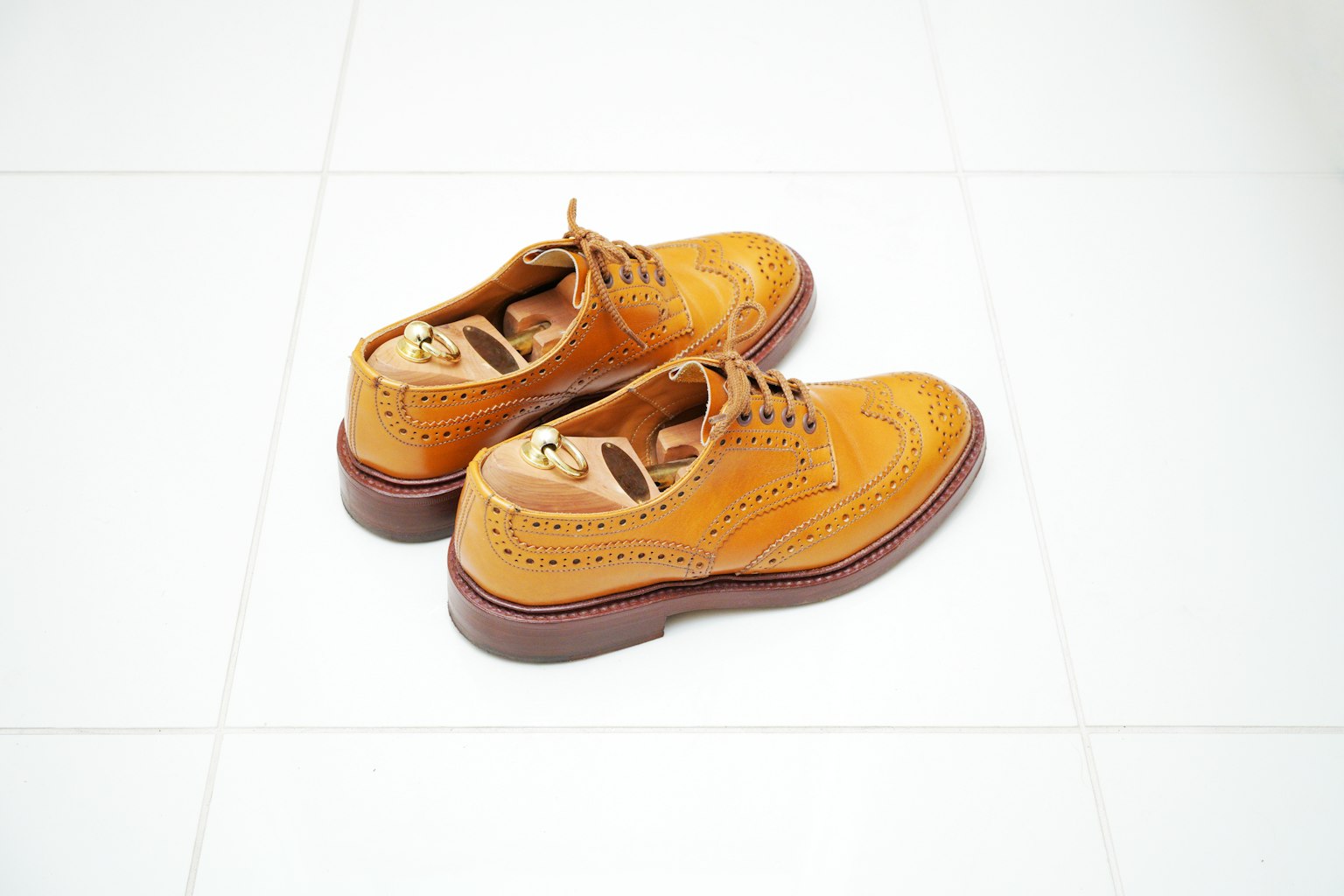 A pair of orange leather shoes placed on white tiles