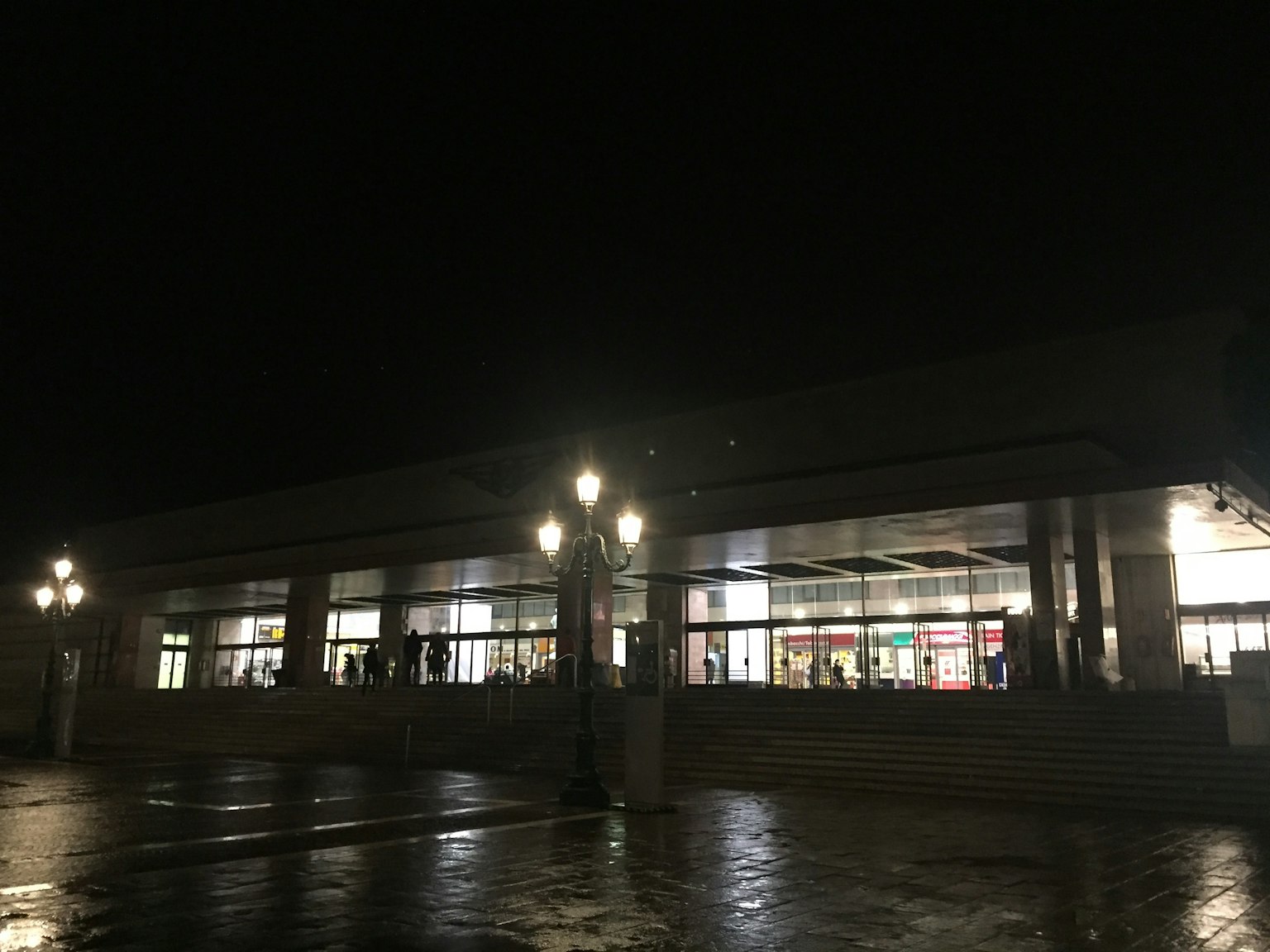 Exterior of a building illuminated at night with visible reflections on the wet pavement
