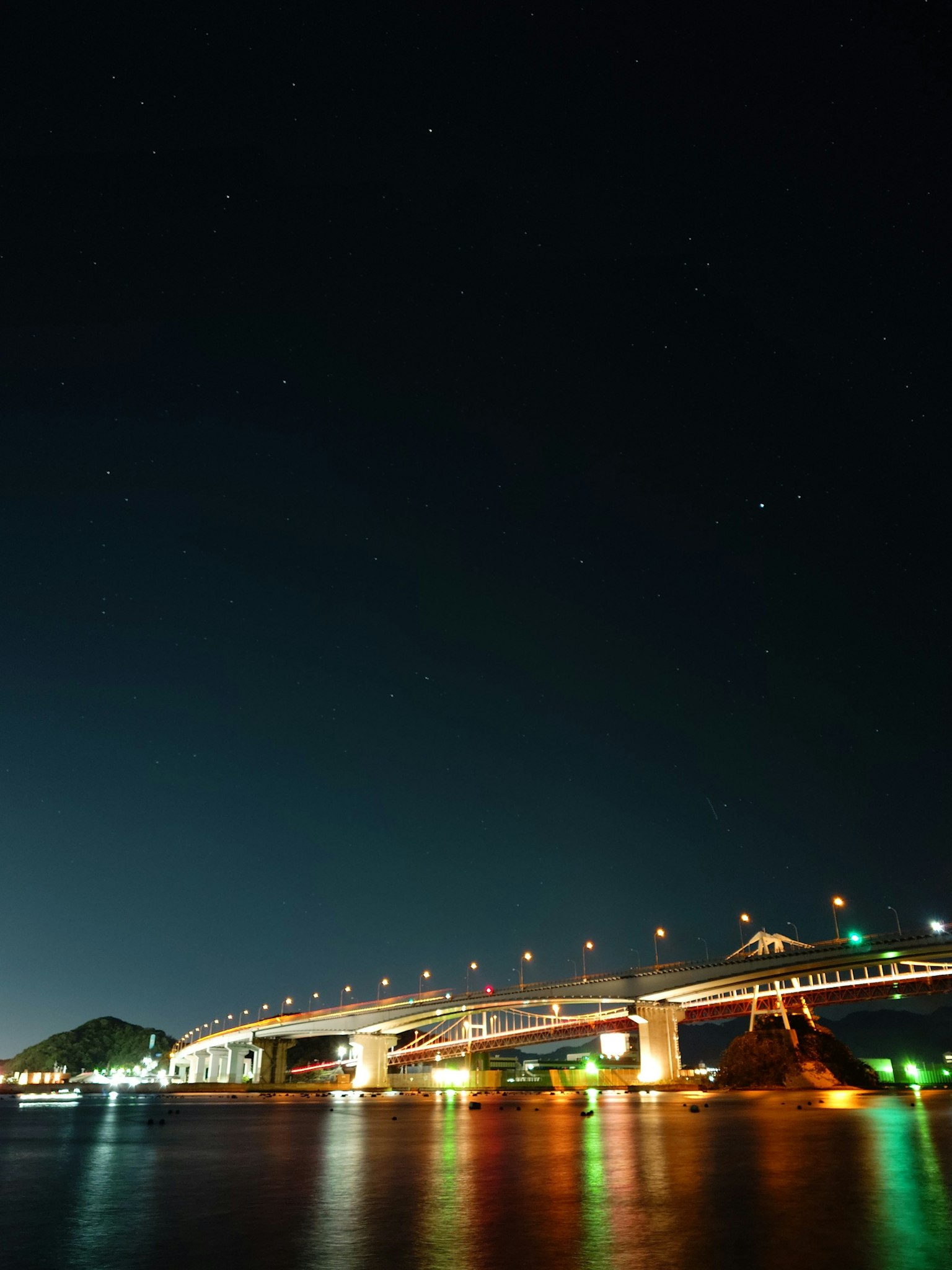 Cảnh cầu được chiếu sáng vào ban đêm với những ngôi sao trên bầu trời và phản chiếu trên mặt nước