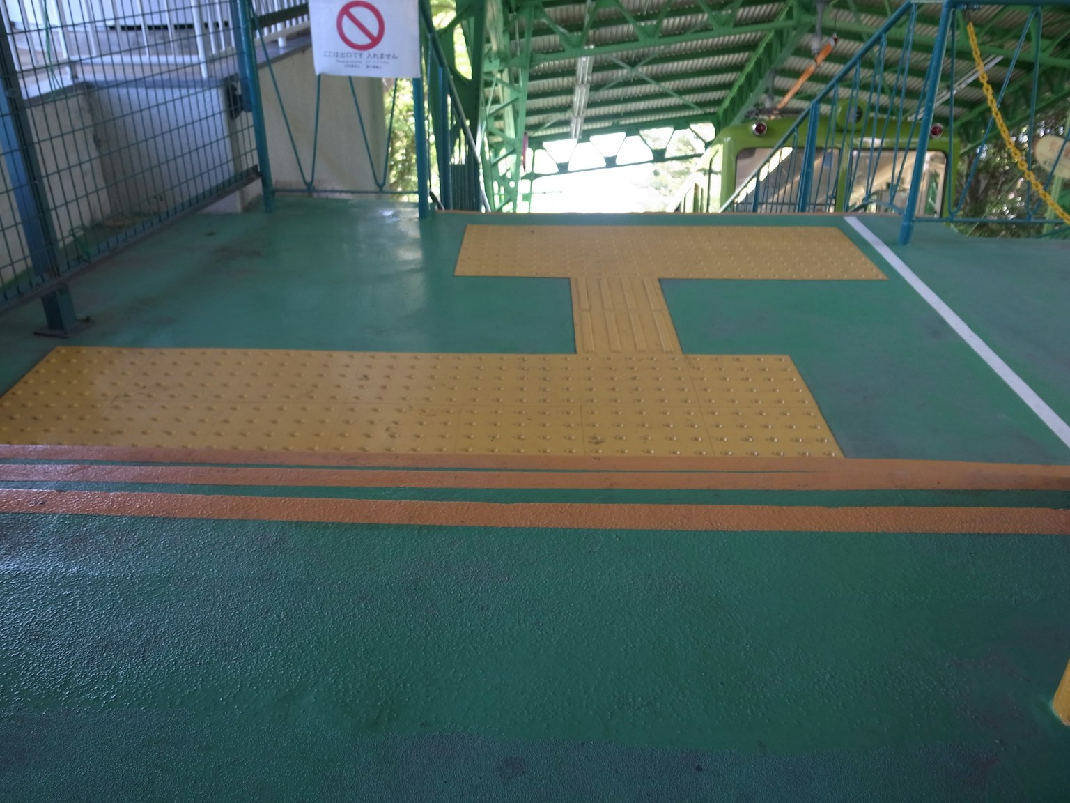 Suelo verde con líneas naranjas y pavimento táctil cerca de una escalera