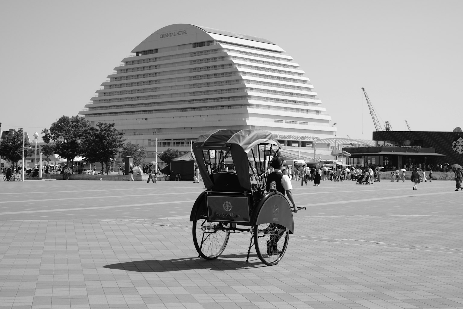 Rikshaw hitam putih di alun-alun dengan bangunan modern di latar belakang