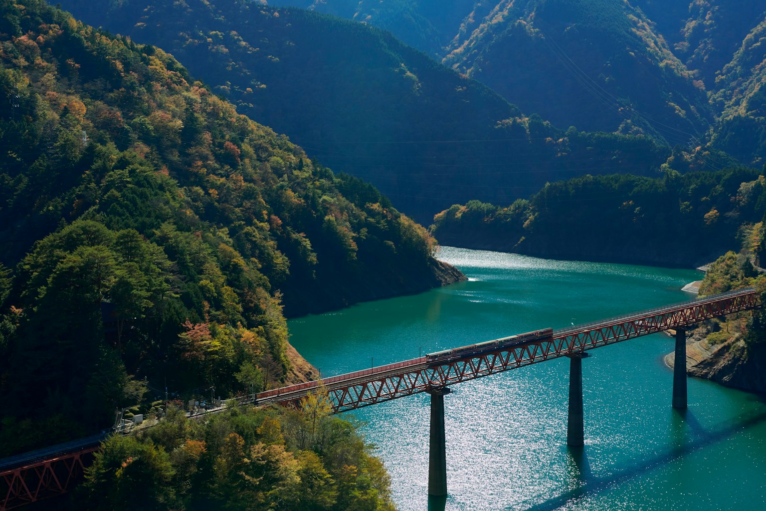 Railway bridge over a green lake surrounded by mountains