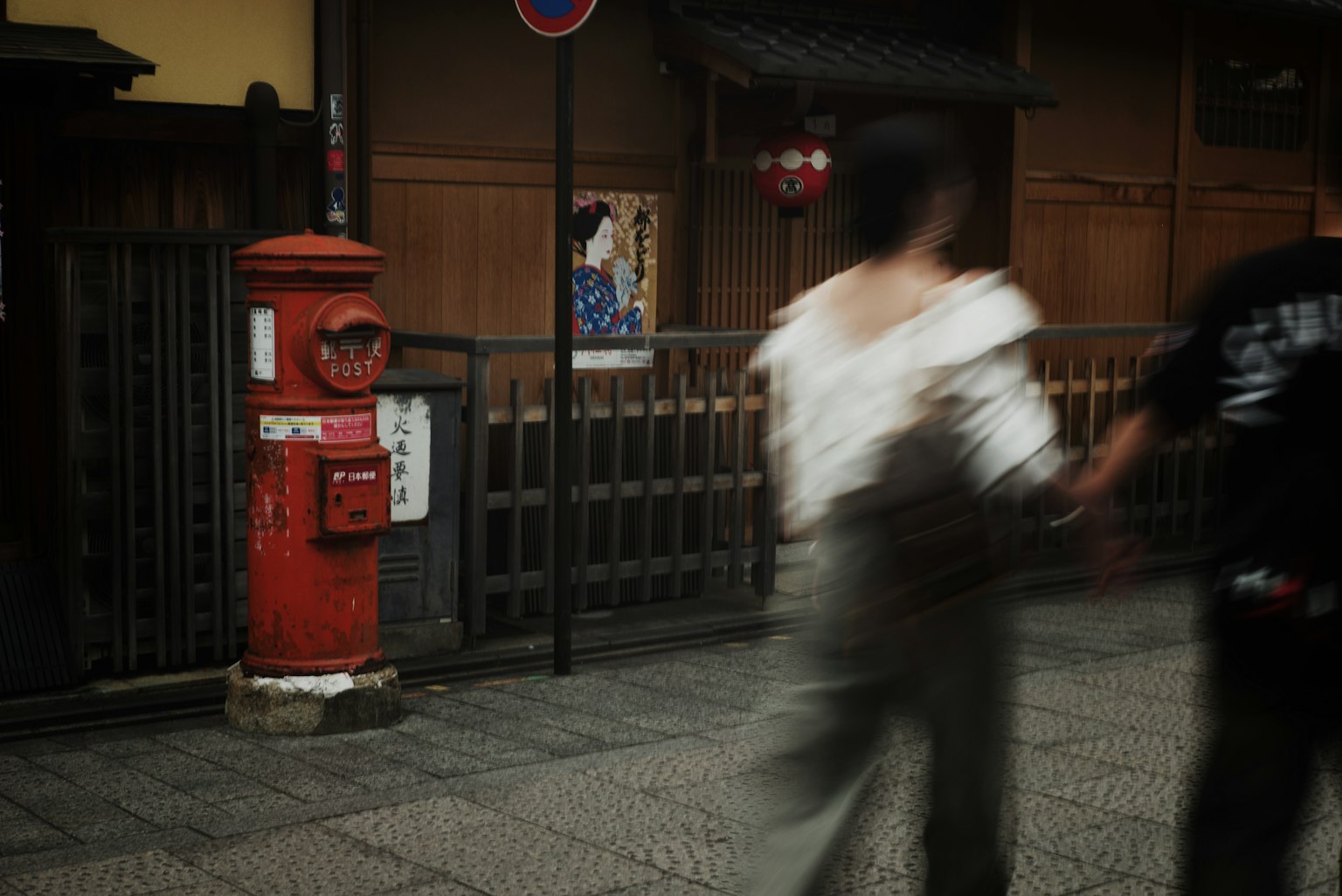Red post box with blurred figures walking in a street scene