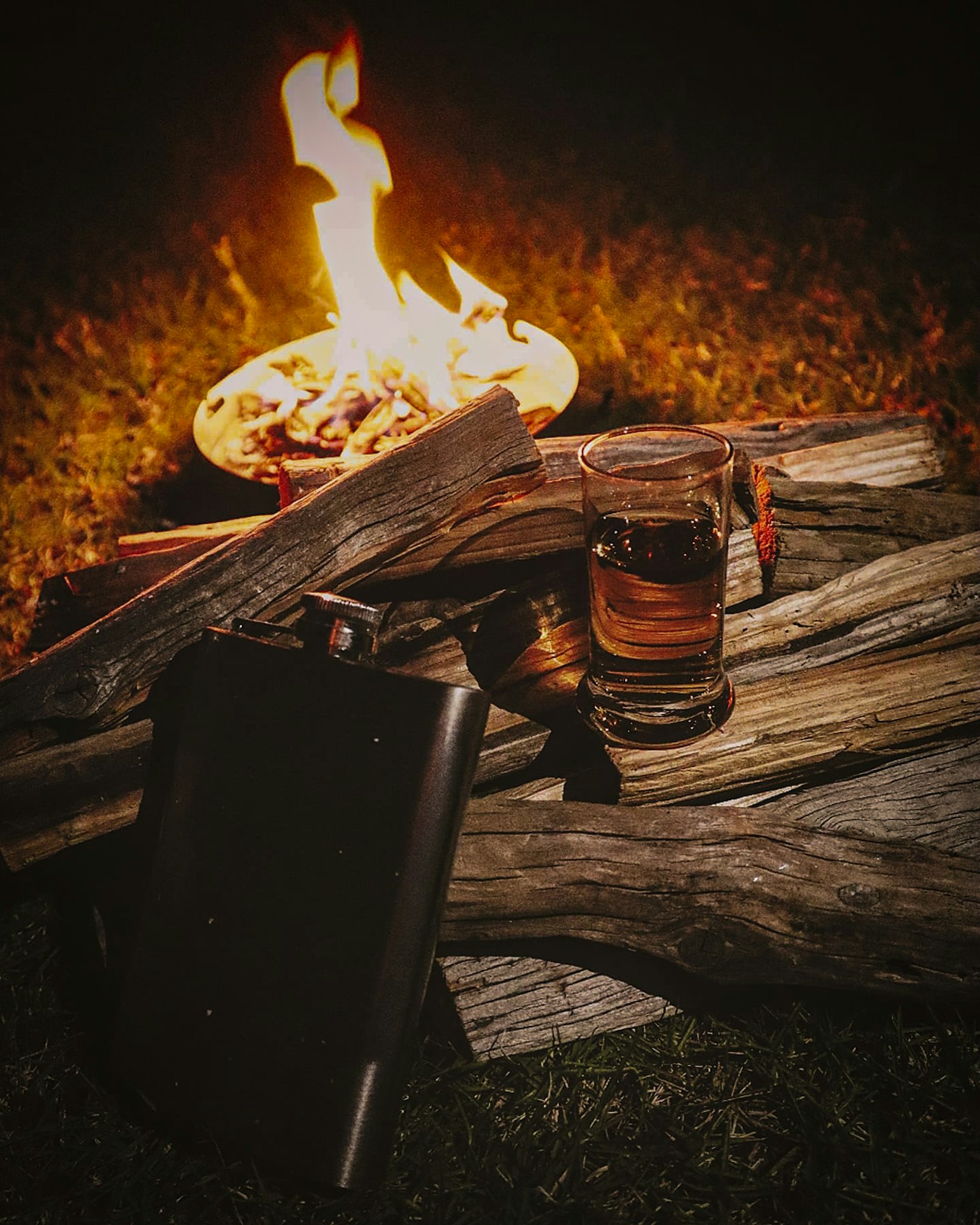 Vaso de whisky y frasco junto a una fogata por la noche