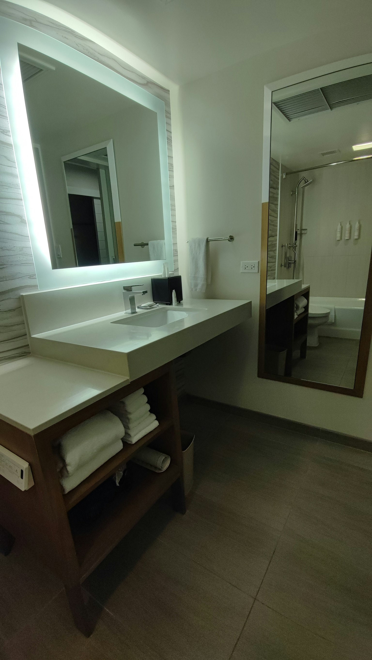 Bagno luminoso con lavabo e grande specchio Asciugamani ordinati su uno scaffale di legno