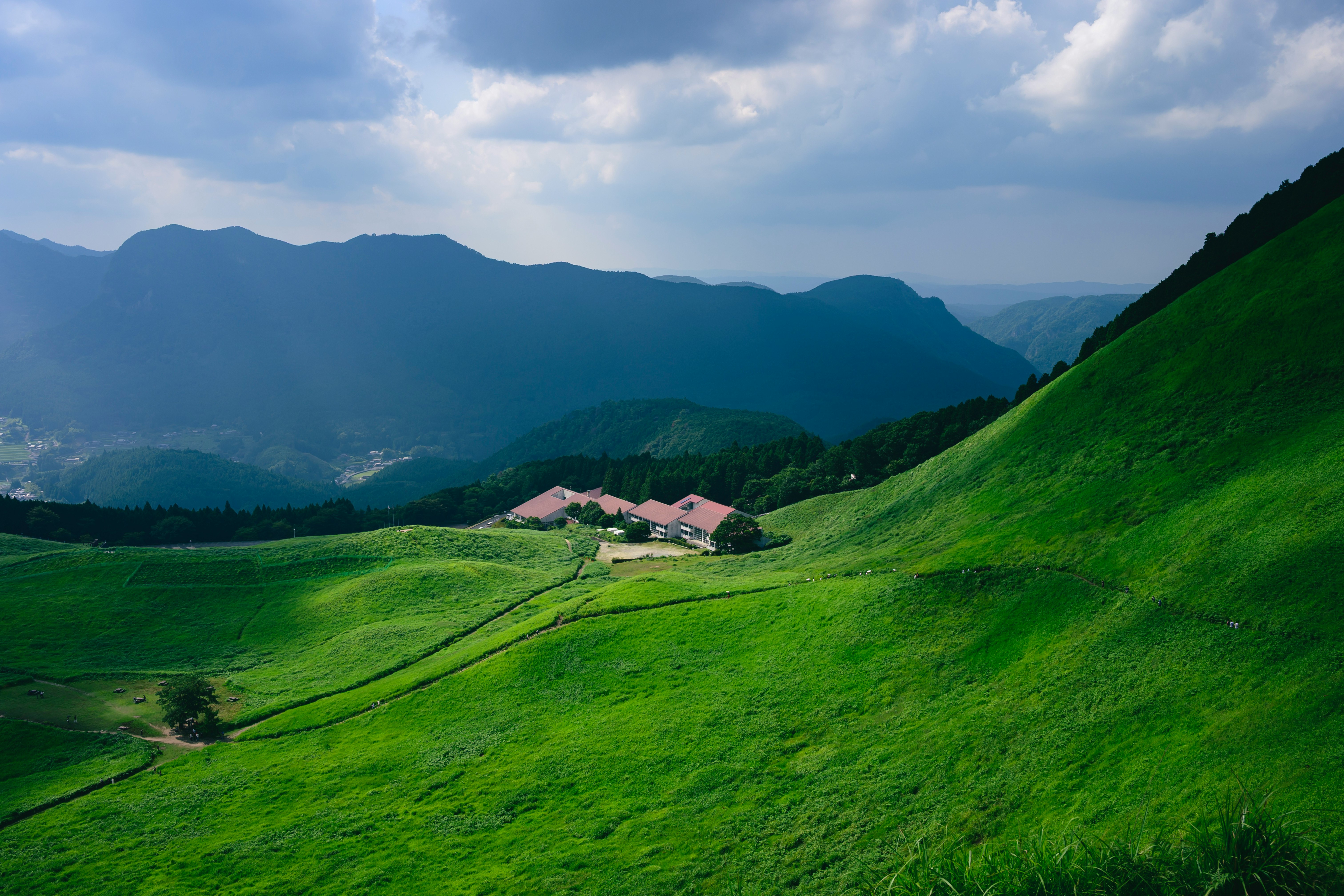 夏の草原に点在する山の家と緑の山並み