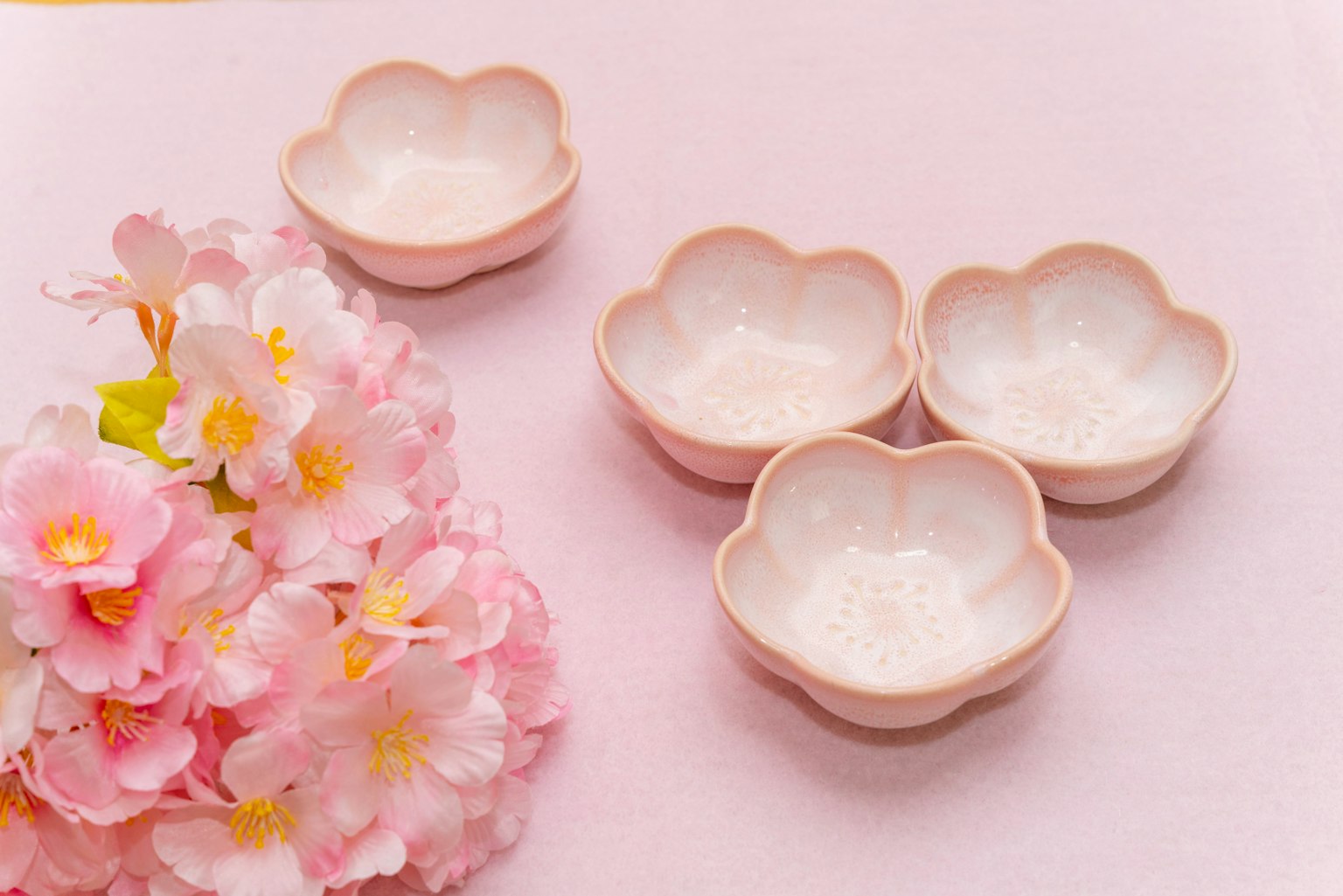 Cuatro cuencos rosas en forma de flor dispuestos junto a un ramo de flores de cerezo