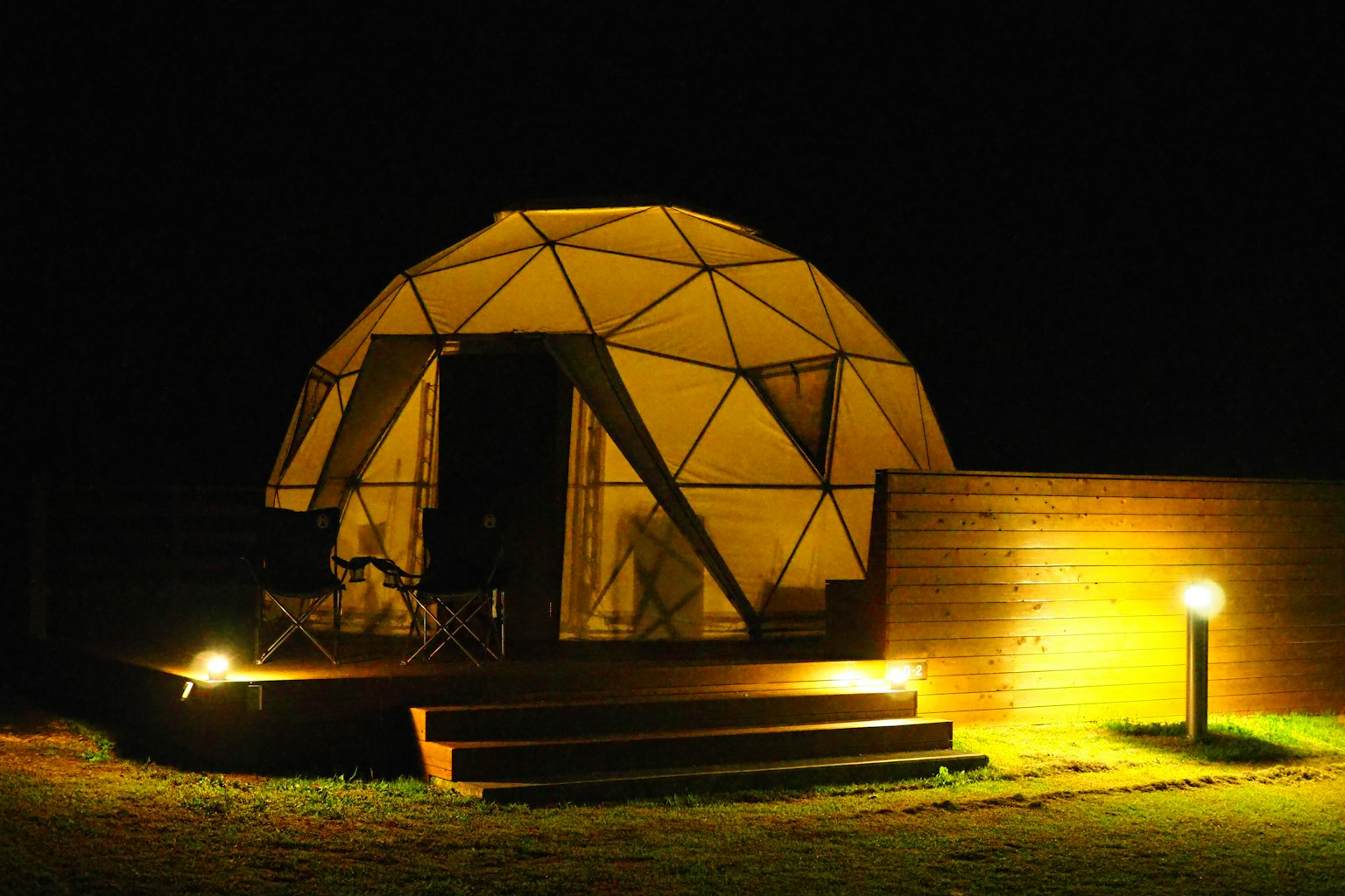 Geodesic dome structure illuminated at night with wooden deck