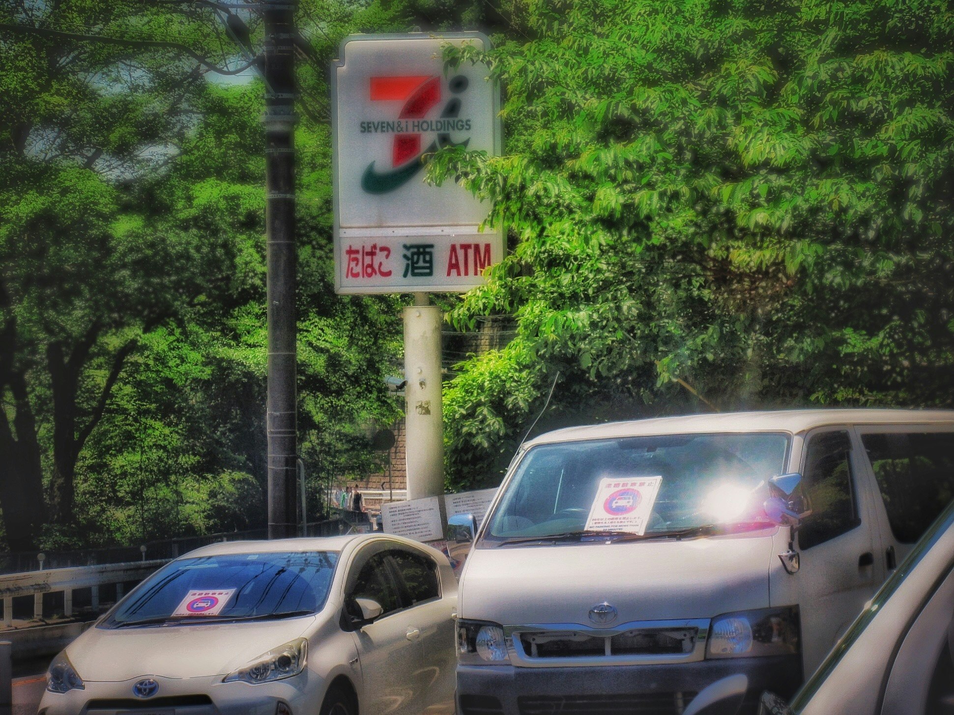 Cars parked at a convenience store parking lot with an ATM sign in Kyoto