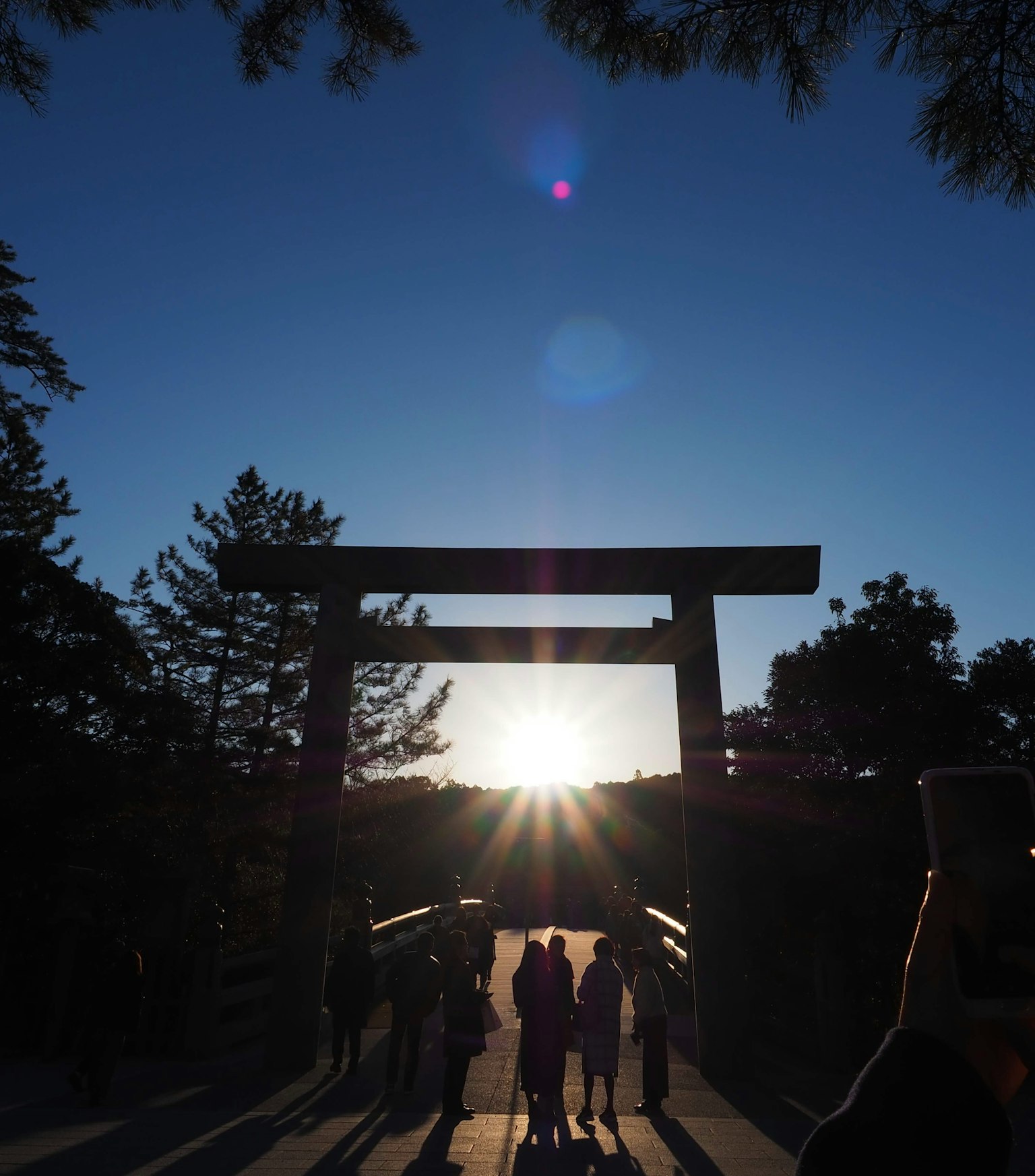Silhouettes of people passing through a torii gate with a sunset in the background