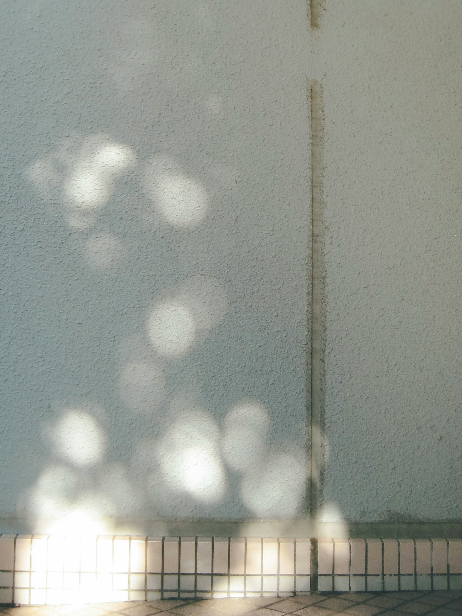 Innenraum mit weißer Wand und gefliestem Boden, Lichtschatten an der Wand
