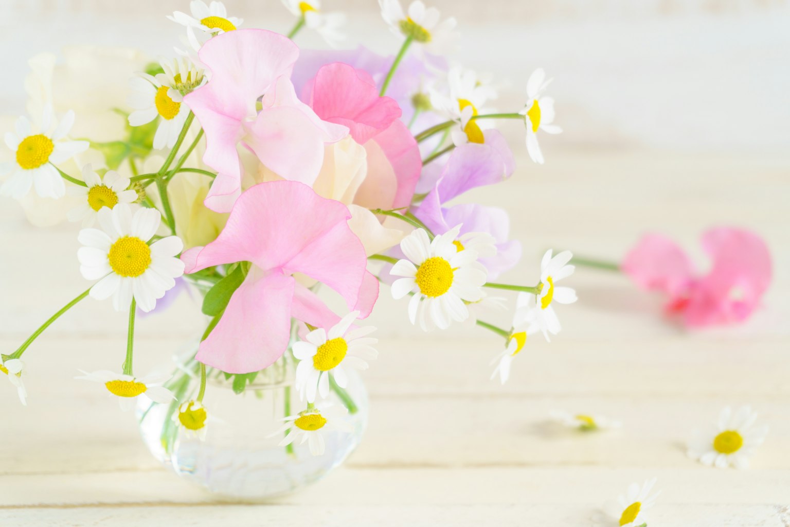 Imagen de un jarrón transparente lleno de flores en tonos pastel