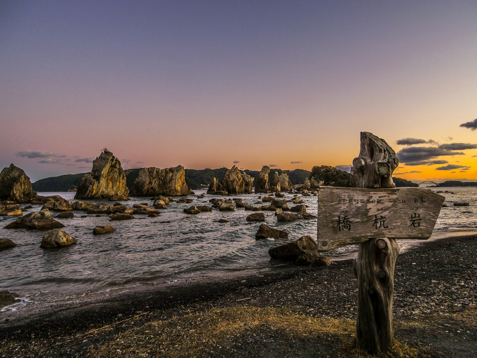 Vecchio cartello sulla spiaggia al tramonto con formazioni rocciose