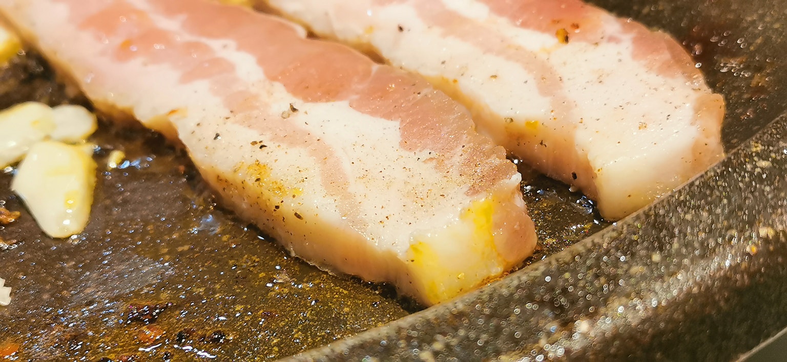 Rebanadas de tocino cocinándose en una sartén