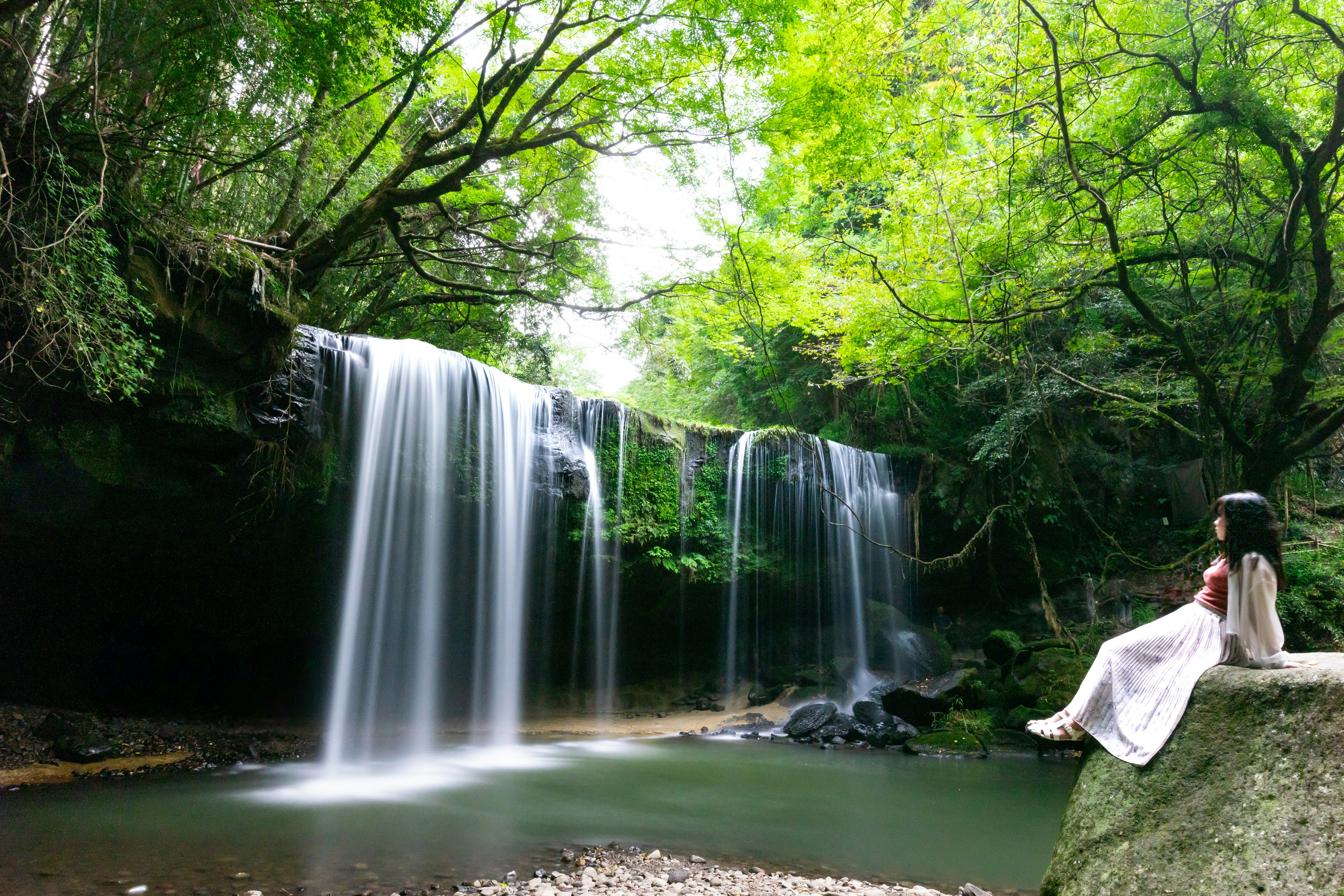 緑の森に囲まれた滝と涼む人の姿