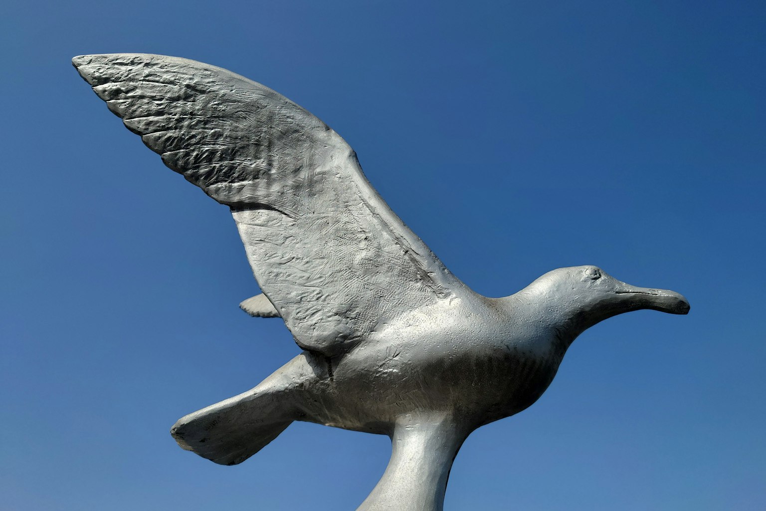 Silberne Vogelskulptur, die gegen einen blauen Himmel schwebt