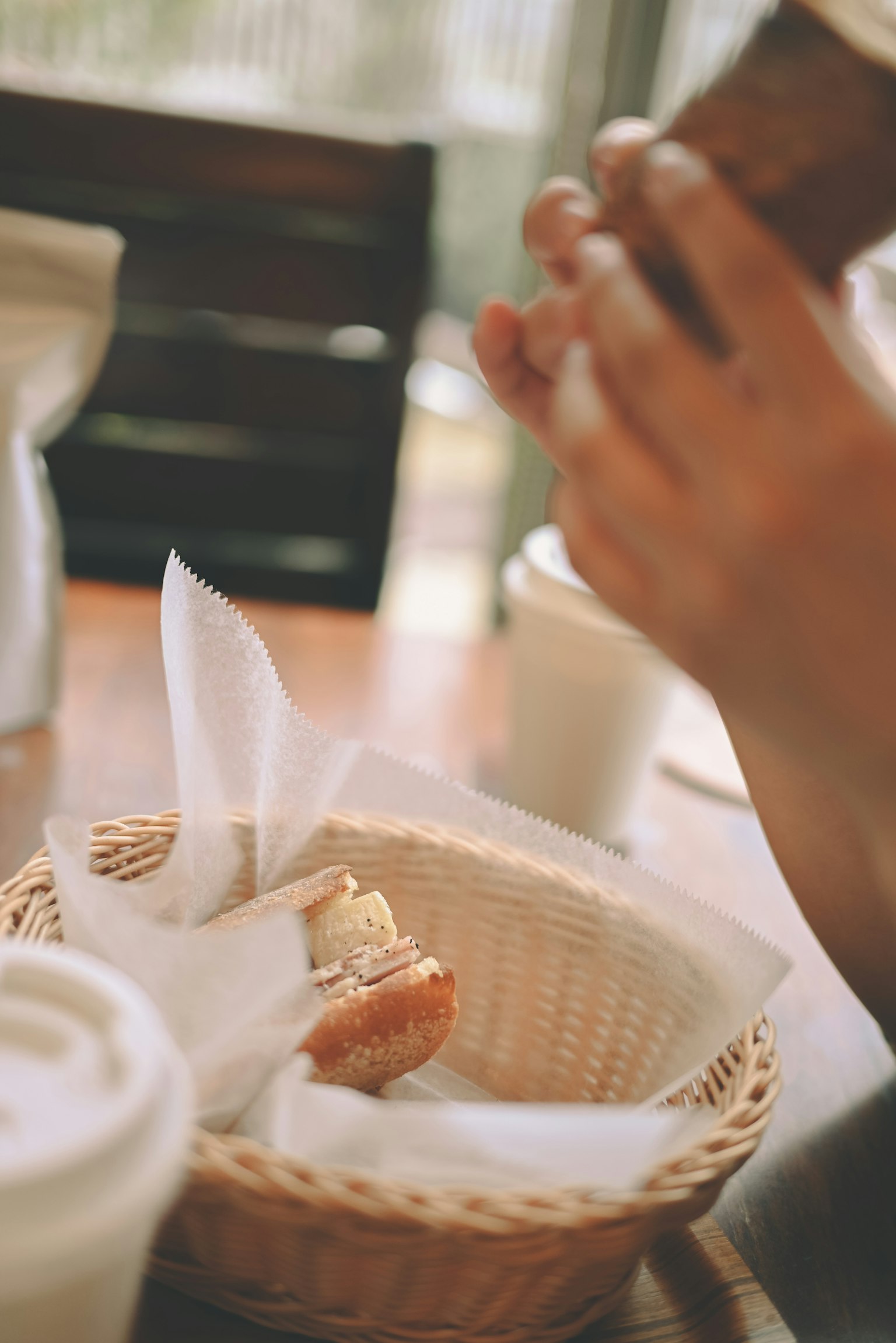 Một bàn tay cầm máy ảnh trên một giỏ bánh mì trên bàn cà phê
