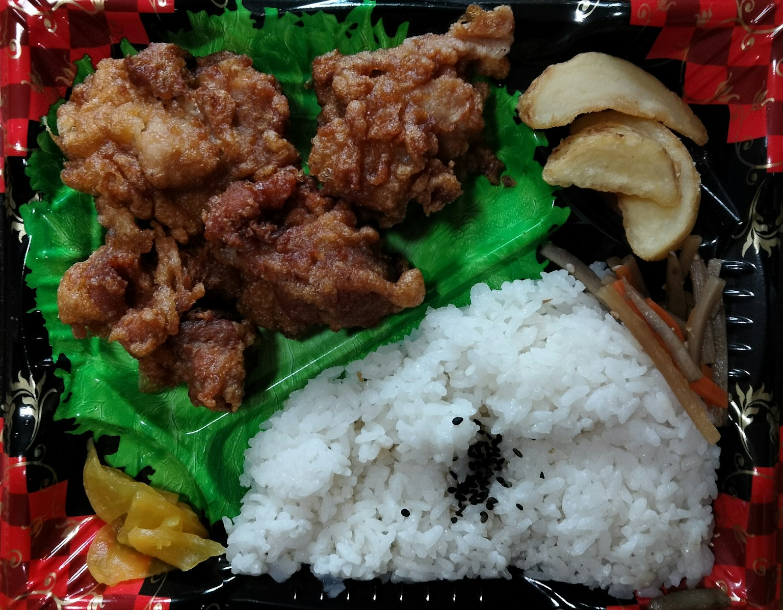 Boîte à bento avec du poulet frit et du riz disposés sur de la laitue verte et des accompagnements