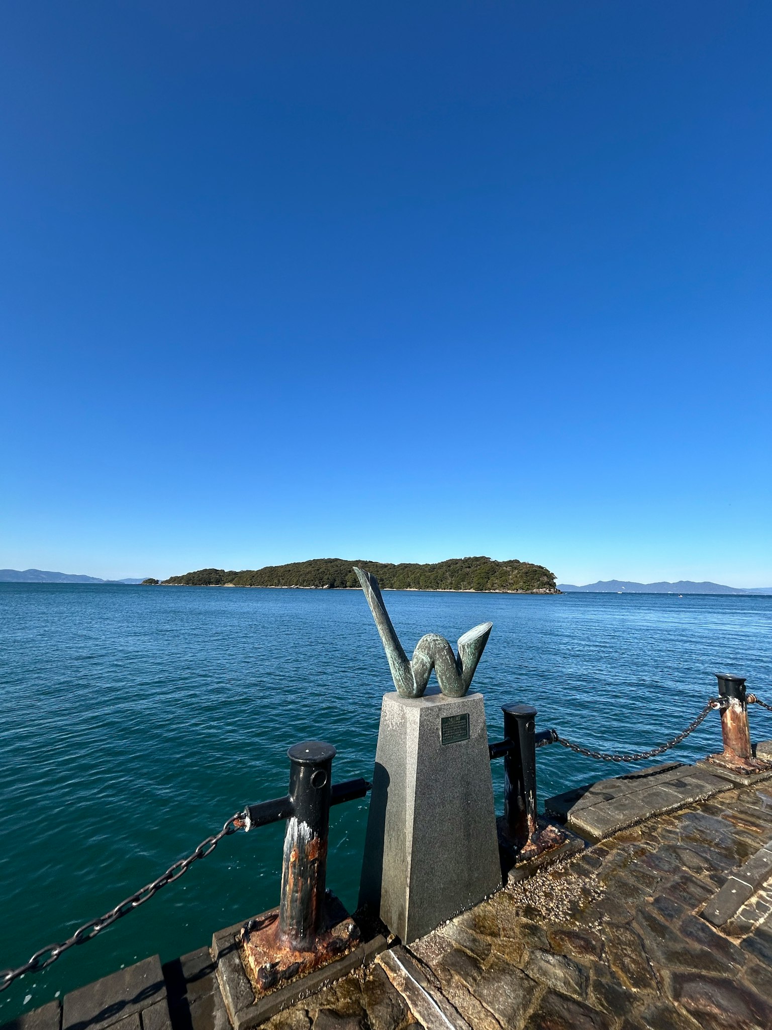 Escultura al final de un muelle con cielo azul claro y mar tranquilo