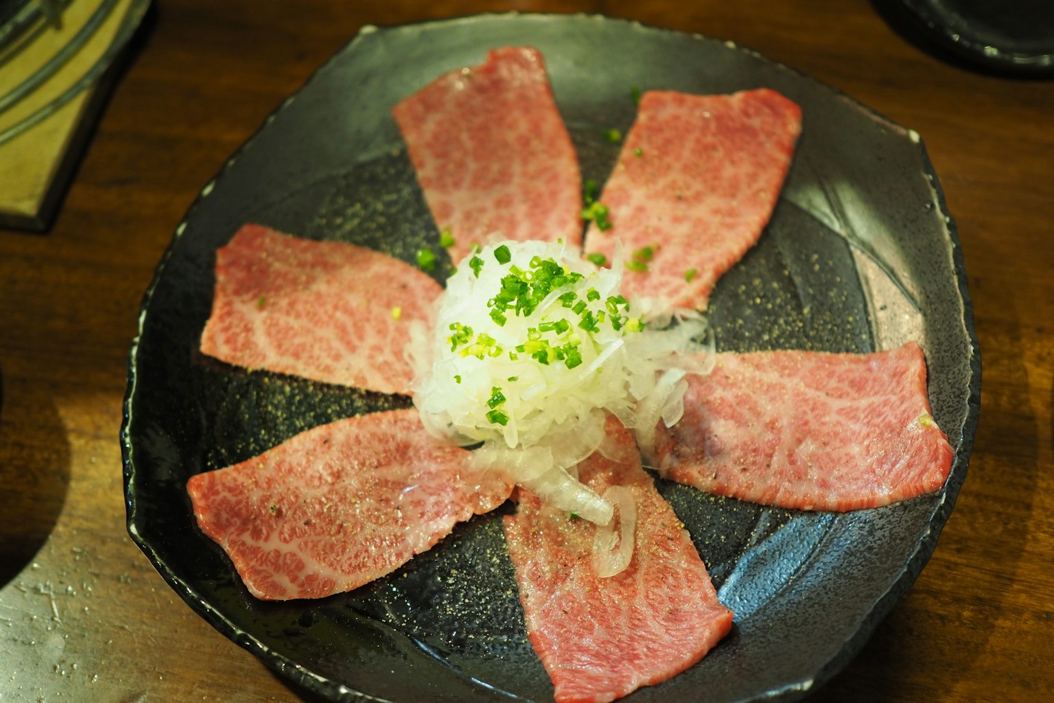 Sliced beef arranged in a flower shape on a black plate with grated radish in the center