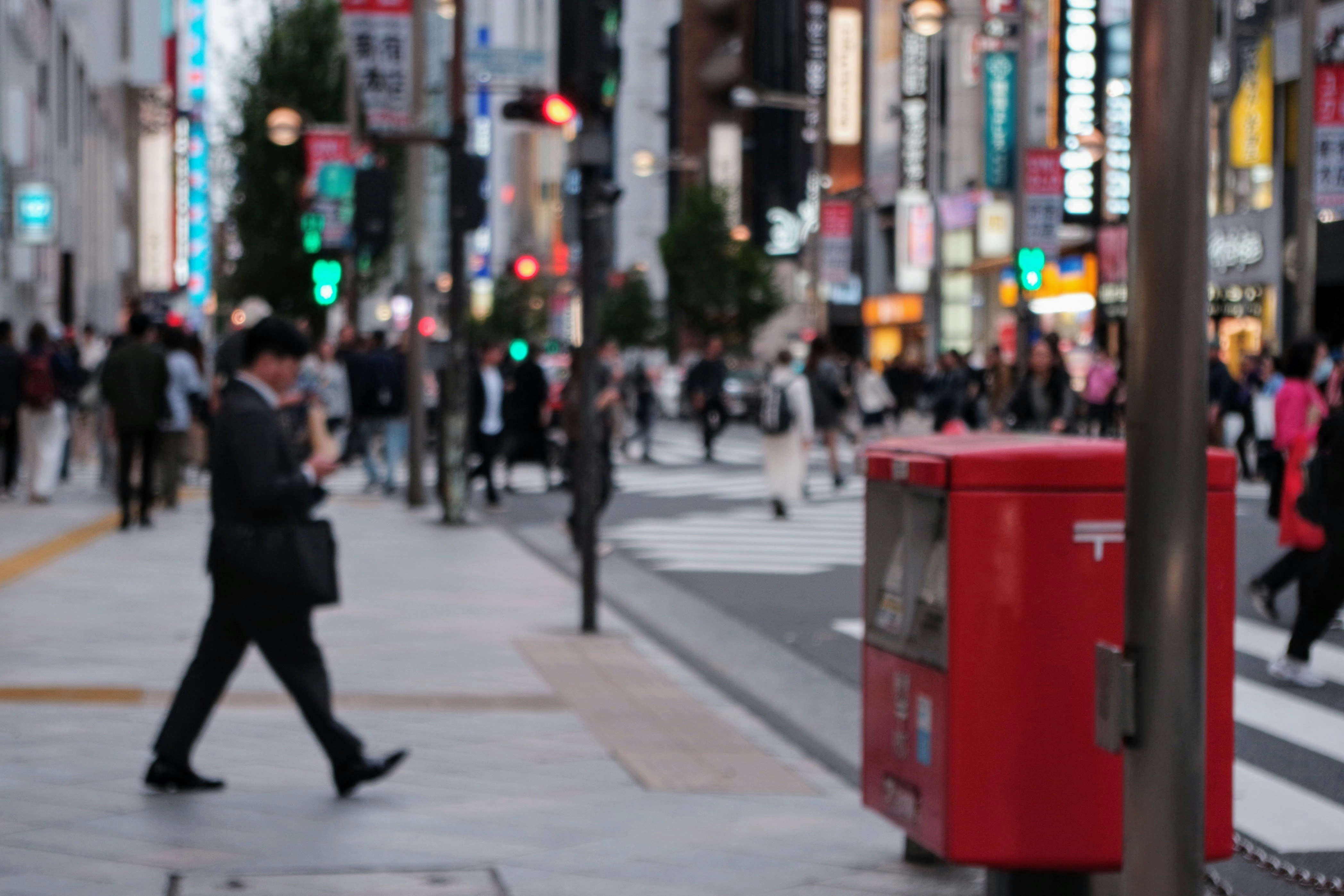 にぎやかな街の歩道を行き交う人々と赤い郵便ポストのある風景