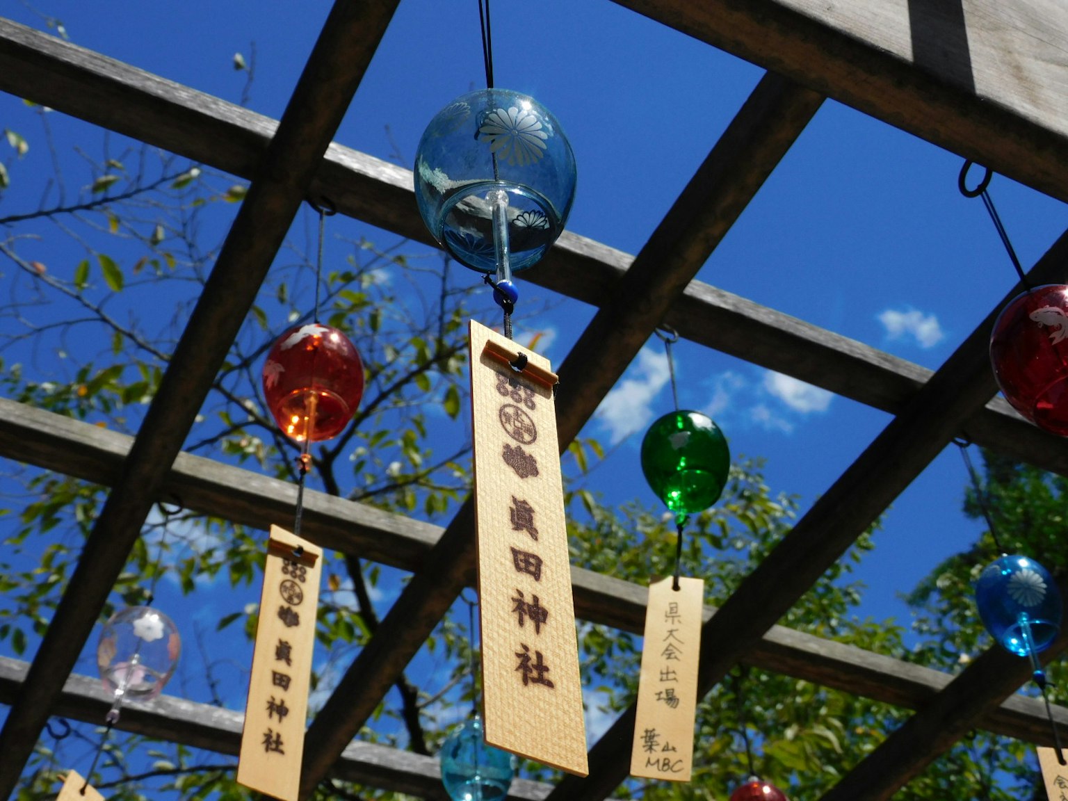Colorful wind chimes and wooden name plaques hanging under a blue sky