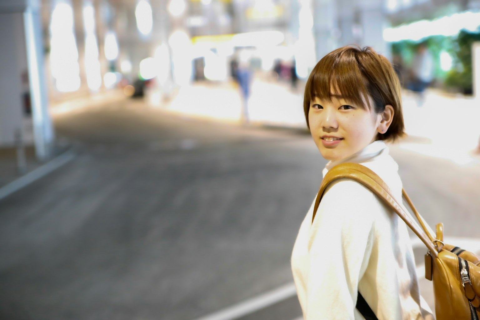 짧은 머리를 가진 흰색 스웨터를 입은 여성이 밤의 도시 거리에서 미소 짓고 있는 모습