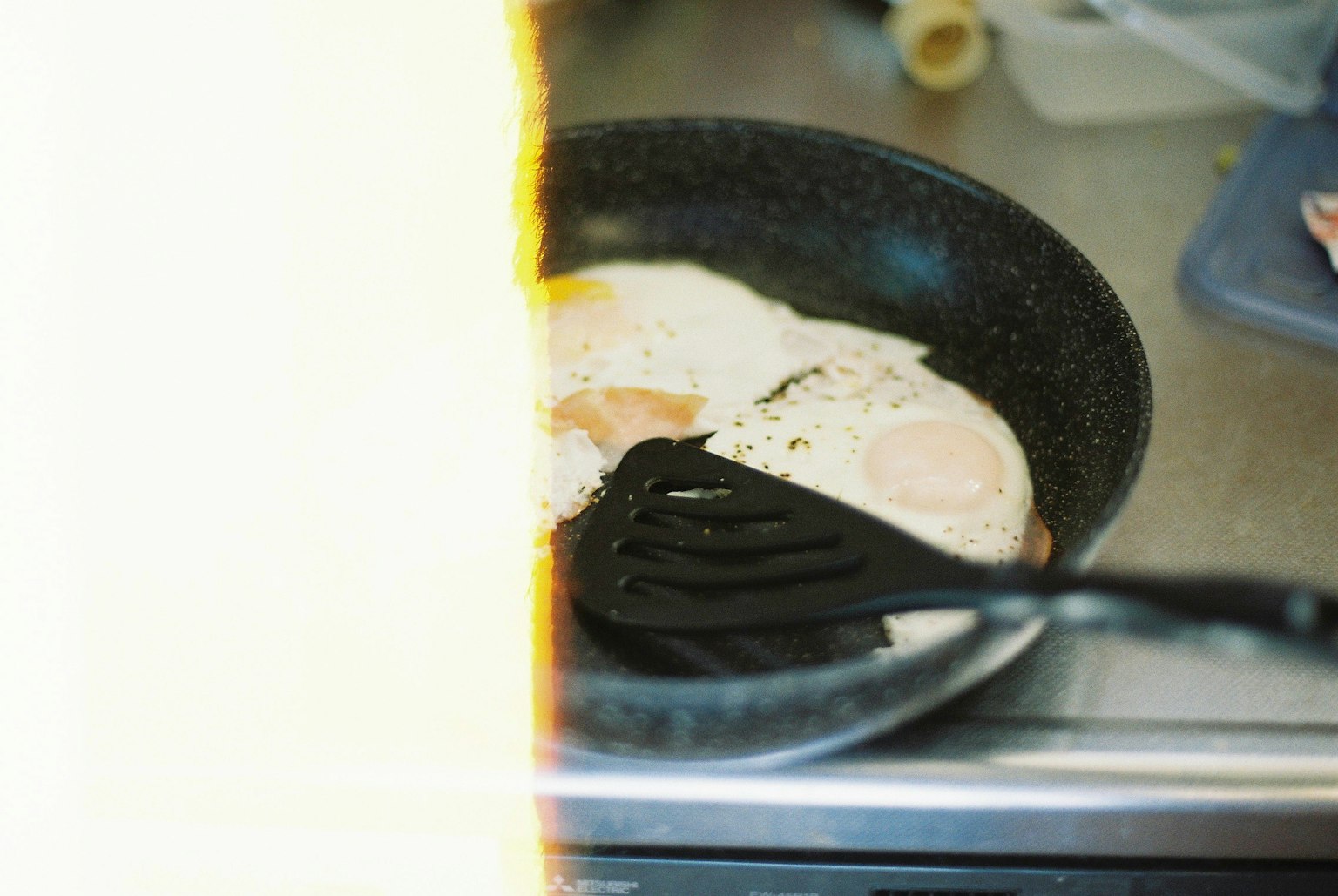 フライパンで焼かれている卵の写真 黒いフライ返しが卵を持ち上げている
