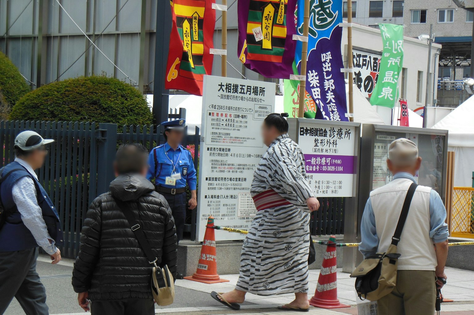 Một đám đông người đi bộ với một người trong trang phục kimono truyền thống và những băng rôn nhiều màu sắc ở phía sau