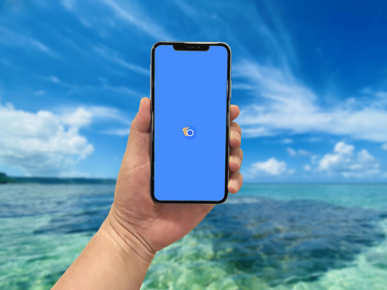 Một bàn tay cầm smartphone với màn hình xanh trước đại dương trong xanh