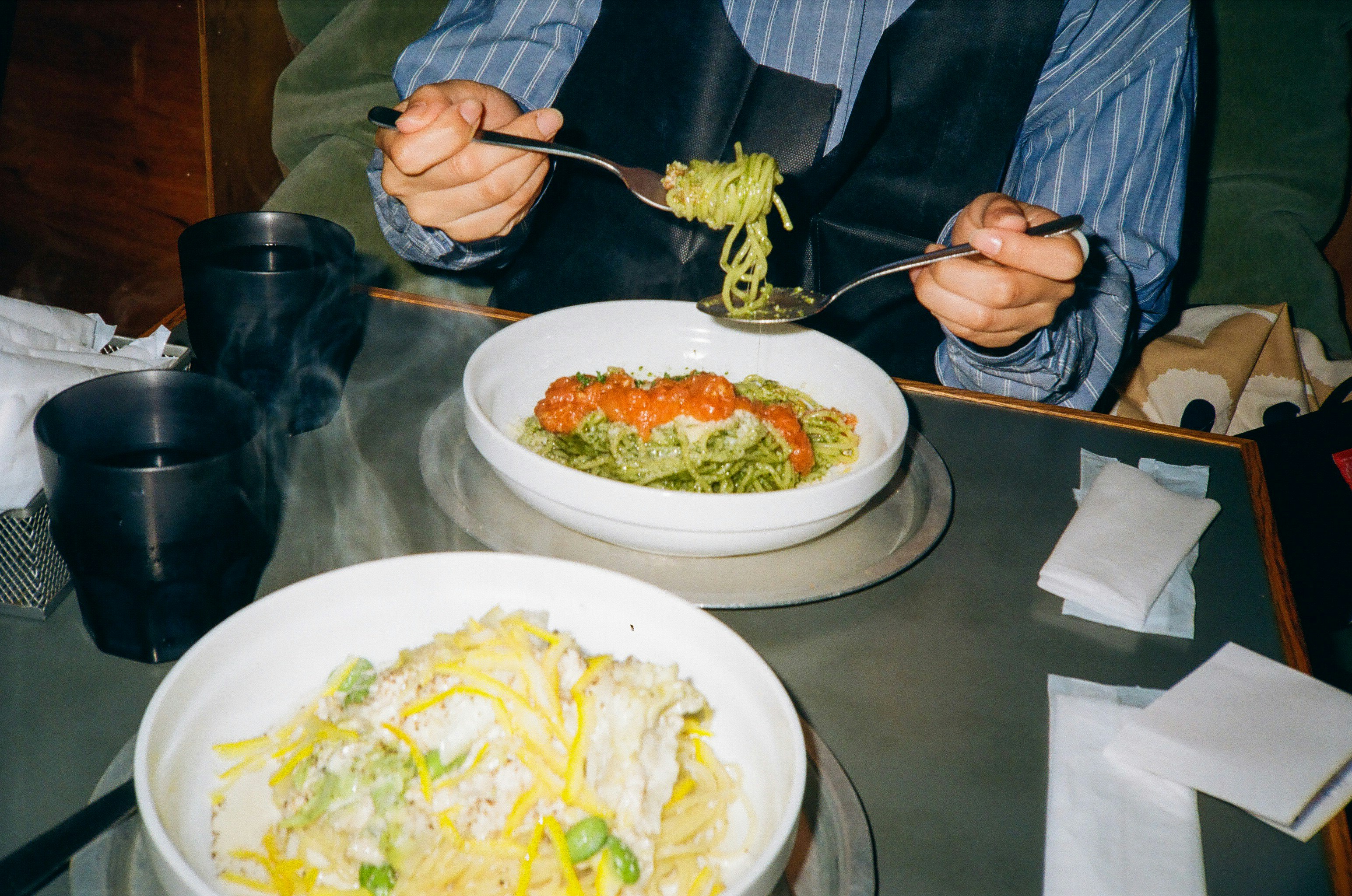 餐桌场景：前景是意面，背景是正在进食的手