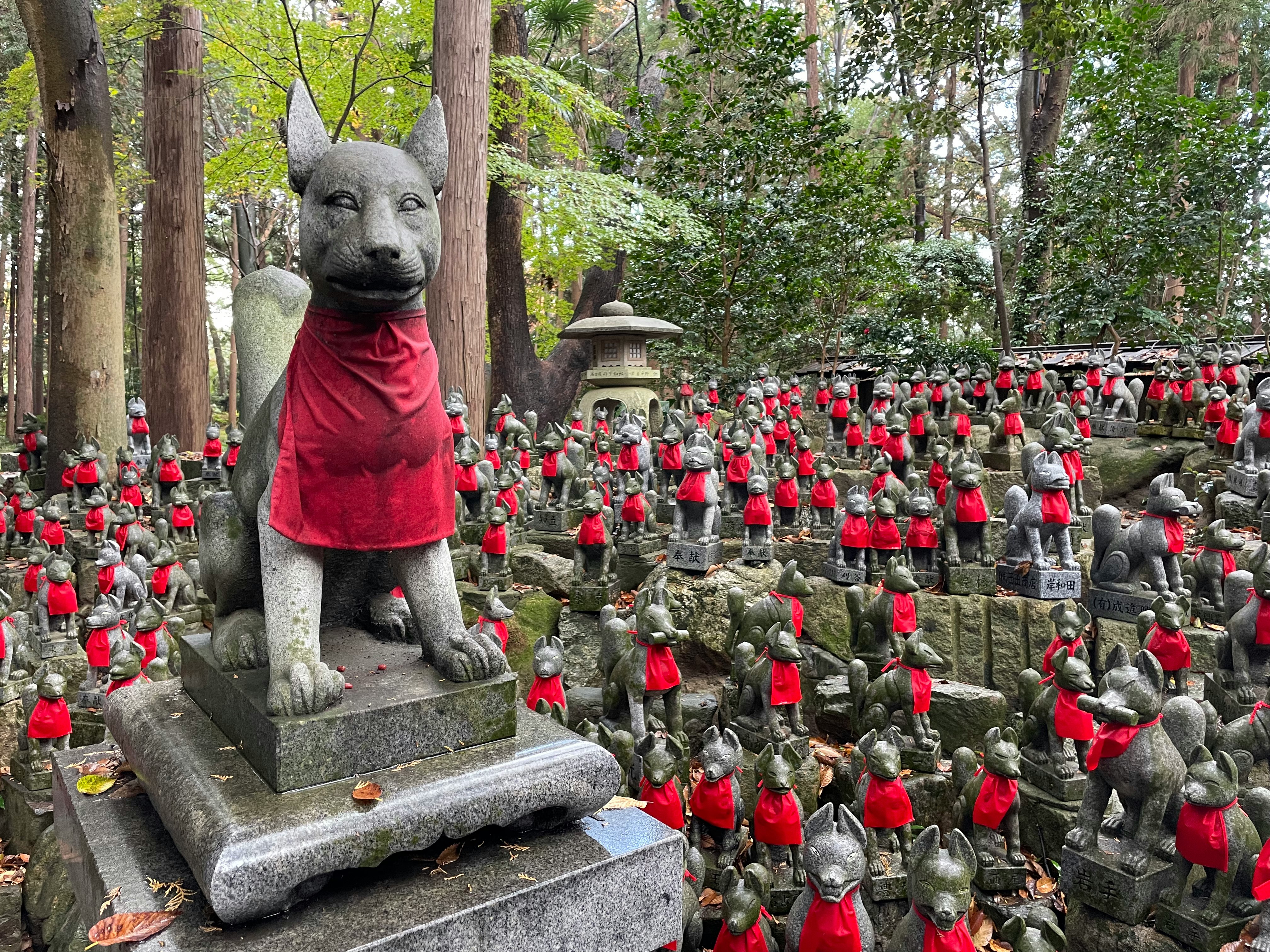 赤い前掛けの小さな置物が並ぶ庭園の石像群