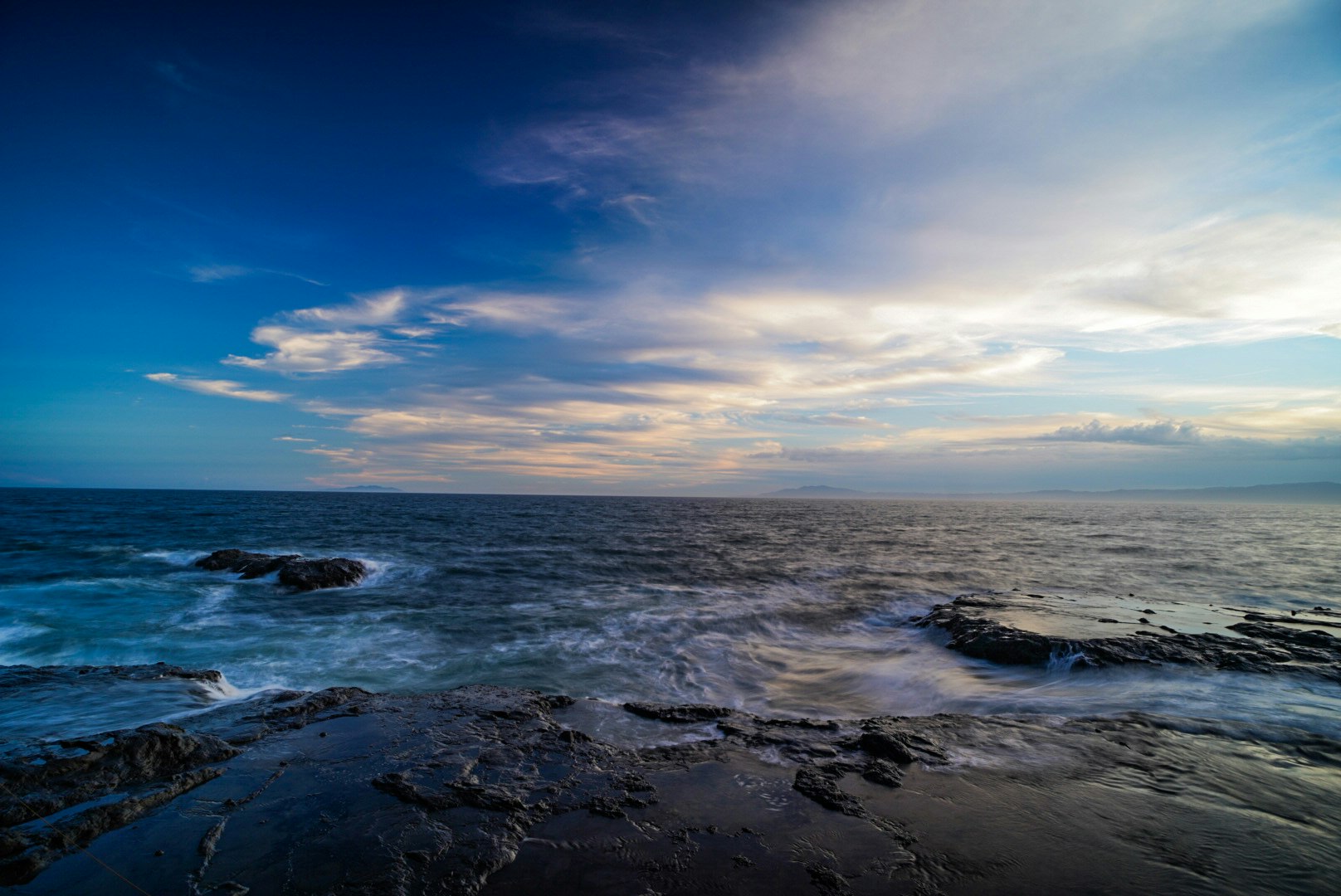 pemandangan laut senja dengan garis pantai berbatu dan cakrawala