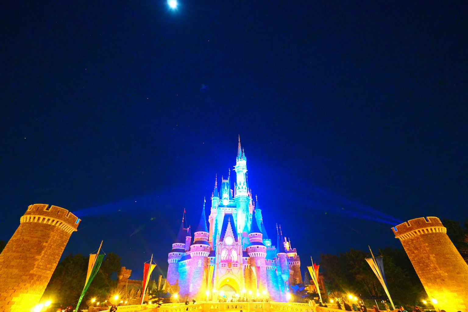 Kastil Disney berwarna yang diterangi di malam hari dengan bulan yang cerah