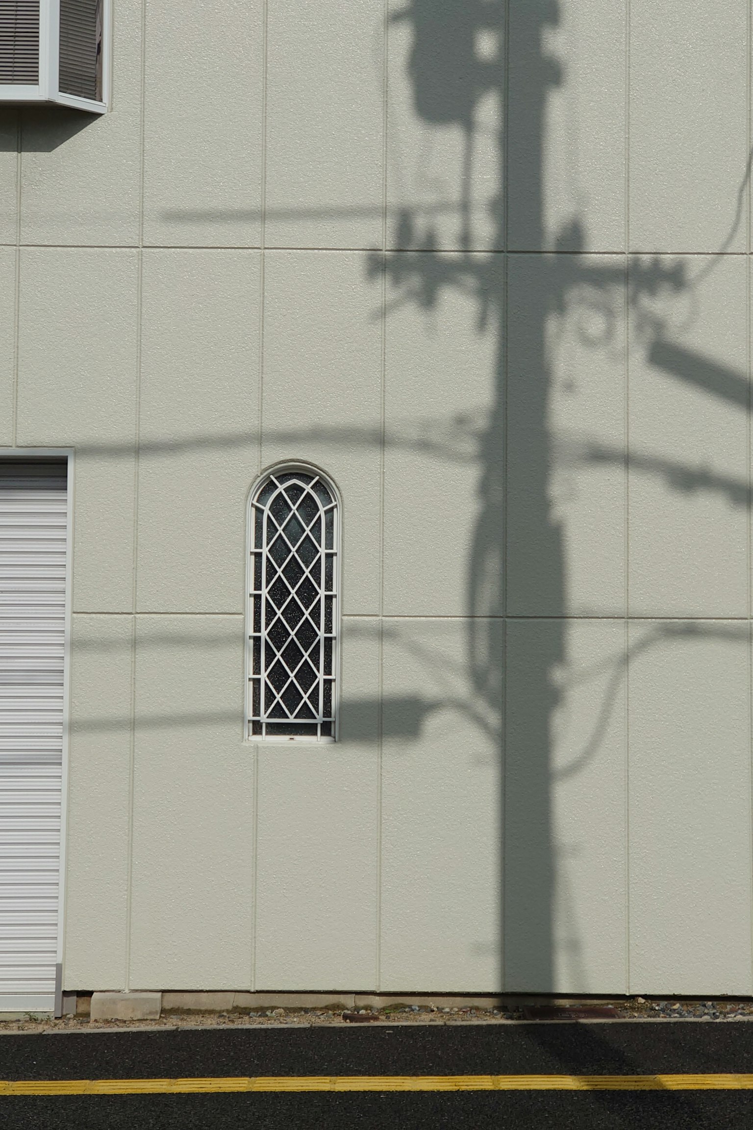 Ombra di un palo elettrico e finestra decorativa su un muro bianco