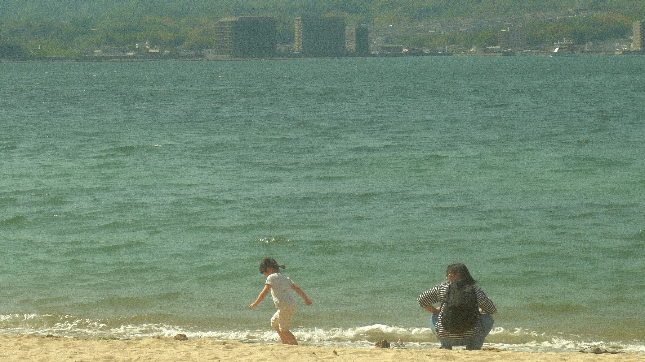 海辺で遊ぶ子どもと海を見つめる人のある風景