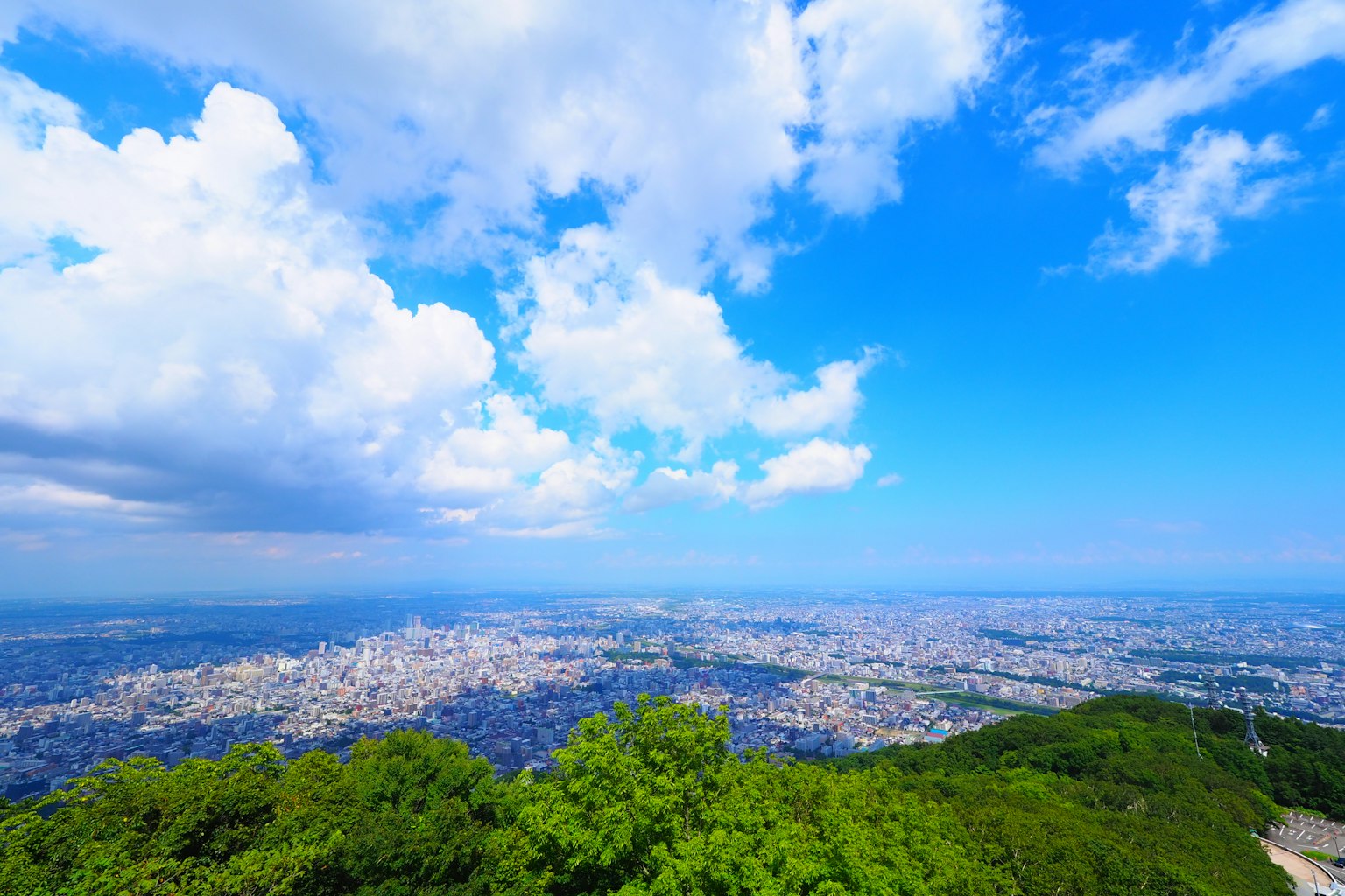 Pemandangan kota yang luas dari puncak gunung hijau dengan langit biru dan awan putih
