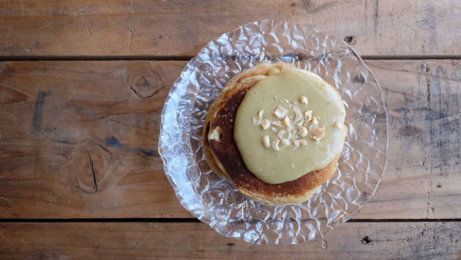 Pancake yang ditutupi krim dan kacang di atas piring kaca di atas meja kayu