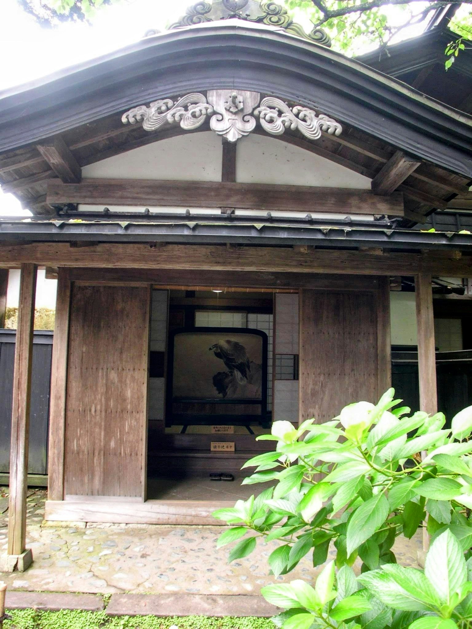 Außenansicht eines traditionellen japanischen Hauses mit Ziegeldach und Holztüren umgeben von Grün