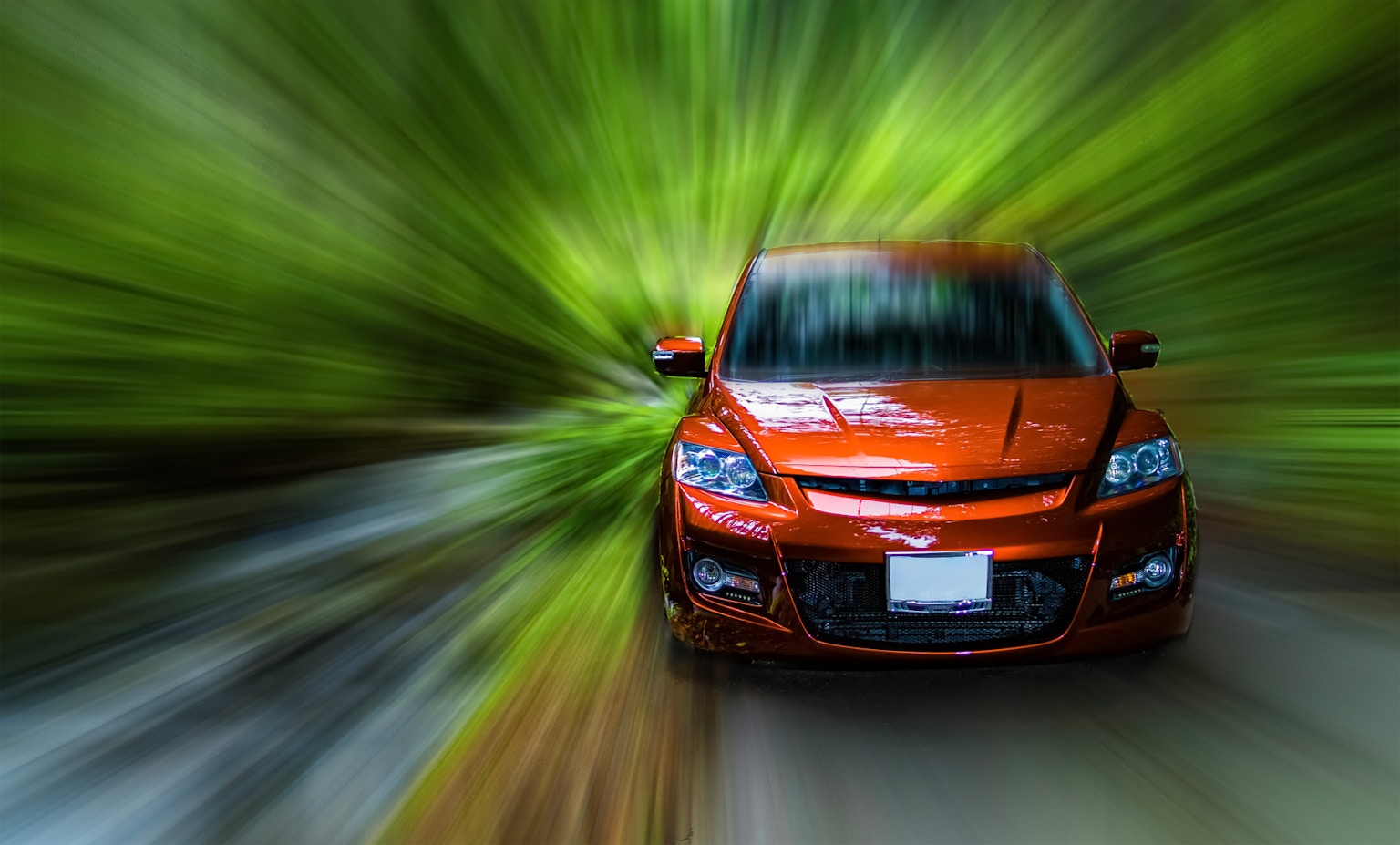 An orange car speeding through a lush green forest