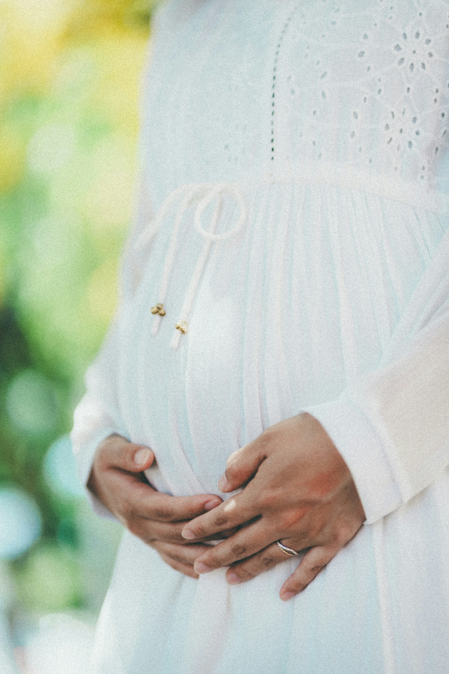Close-up of a pregnant woman in a white dress holding her belly