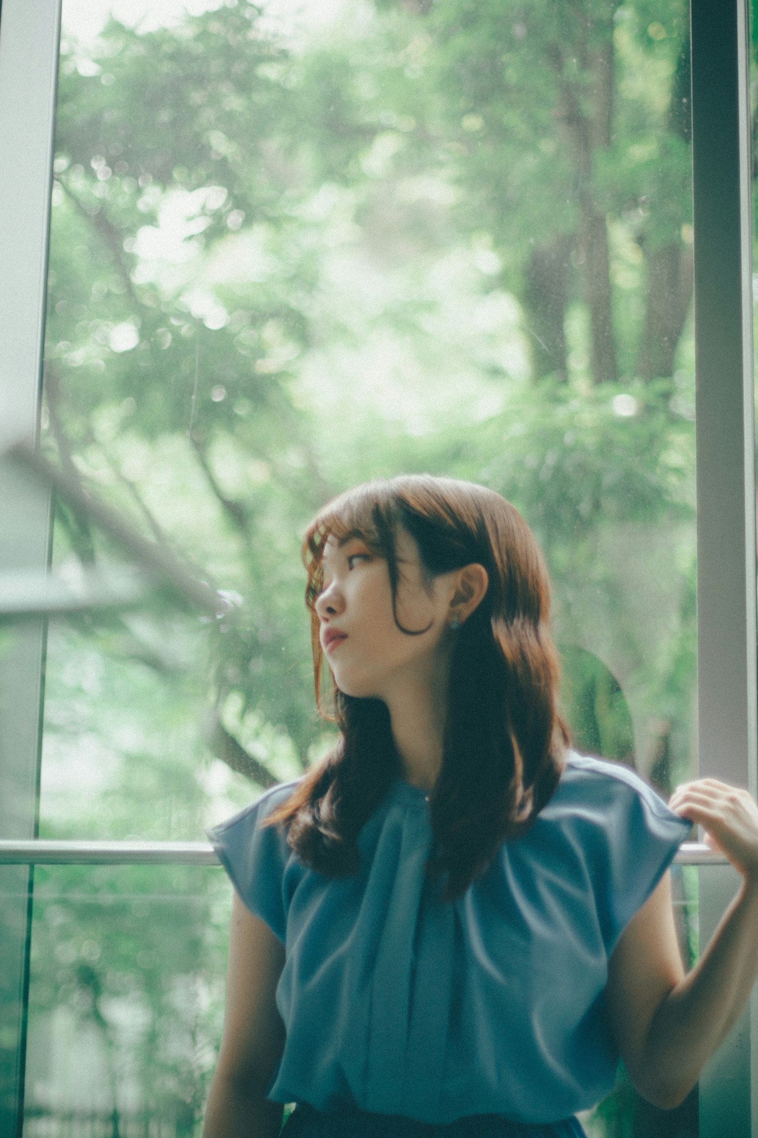 一位穿著藍色襯衫的女性在窗邊向外看