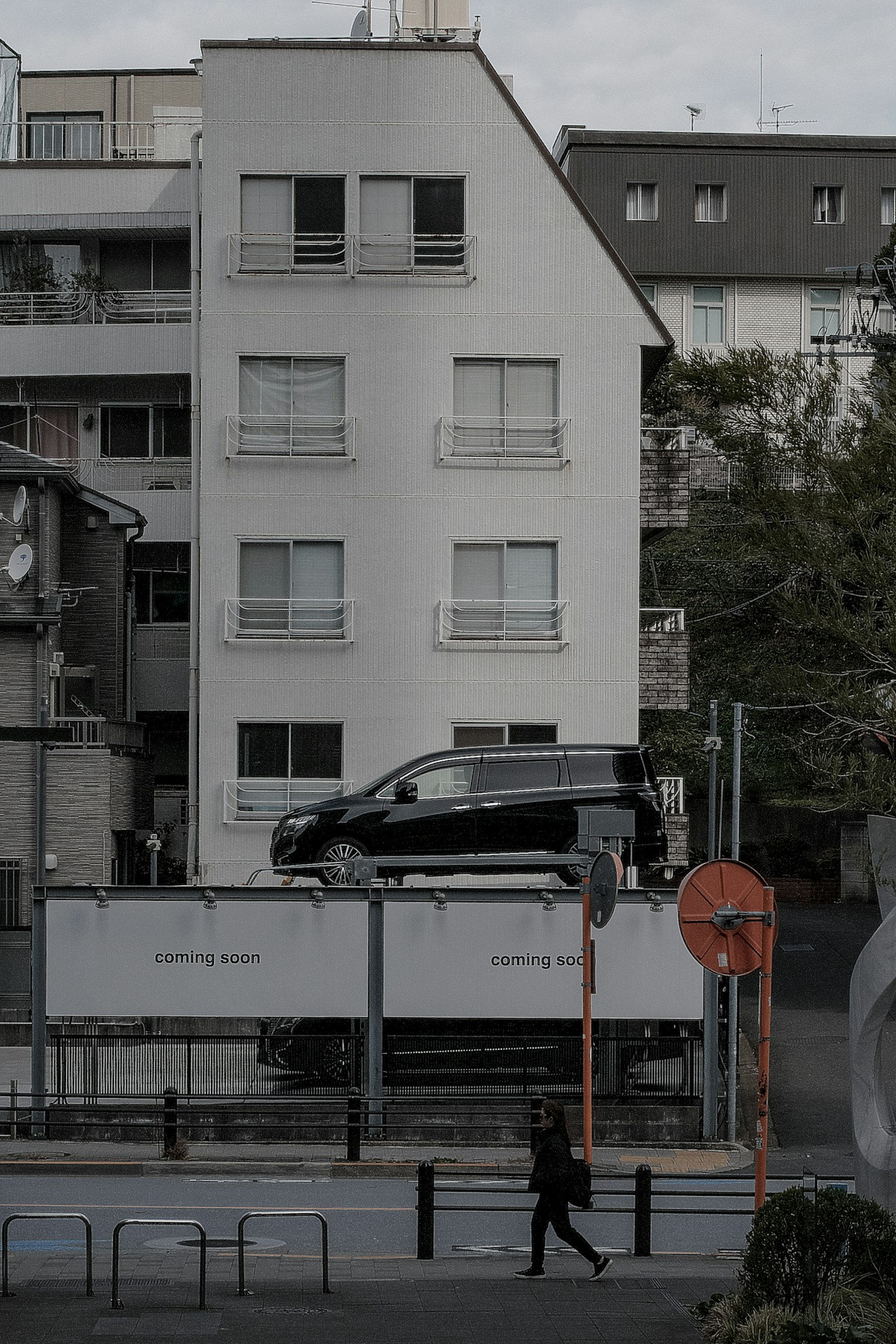 Un coche negro estacionado frente a un edificio blanco con un peatón caminando