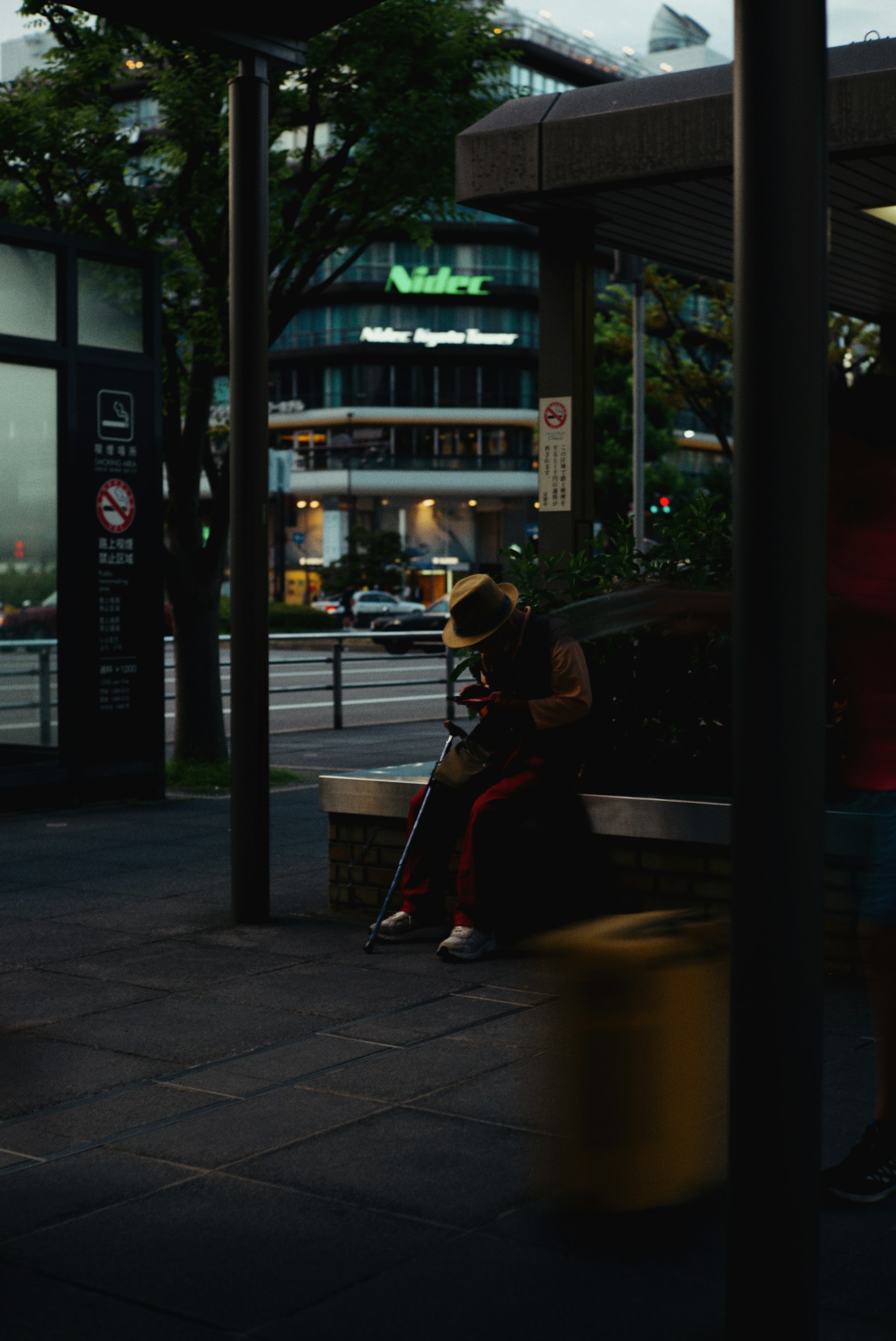 A person sitting at a city bus stop with surrounding buildings