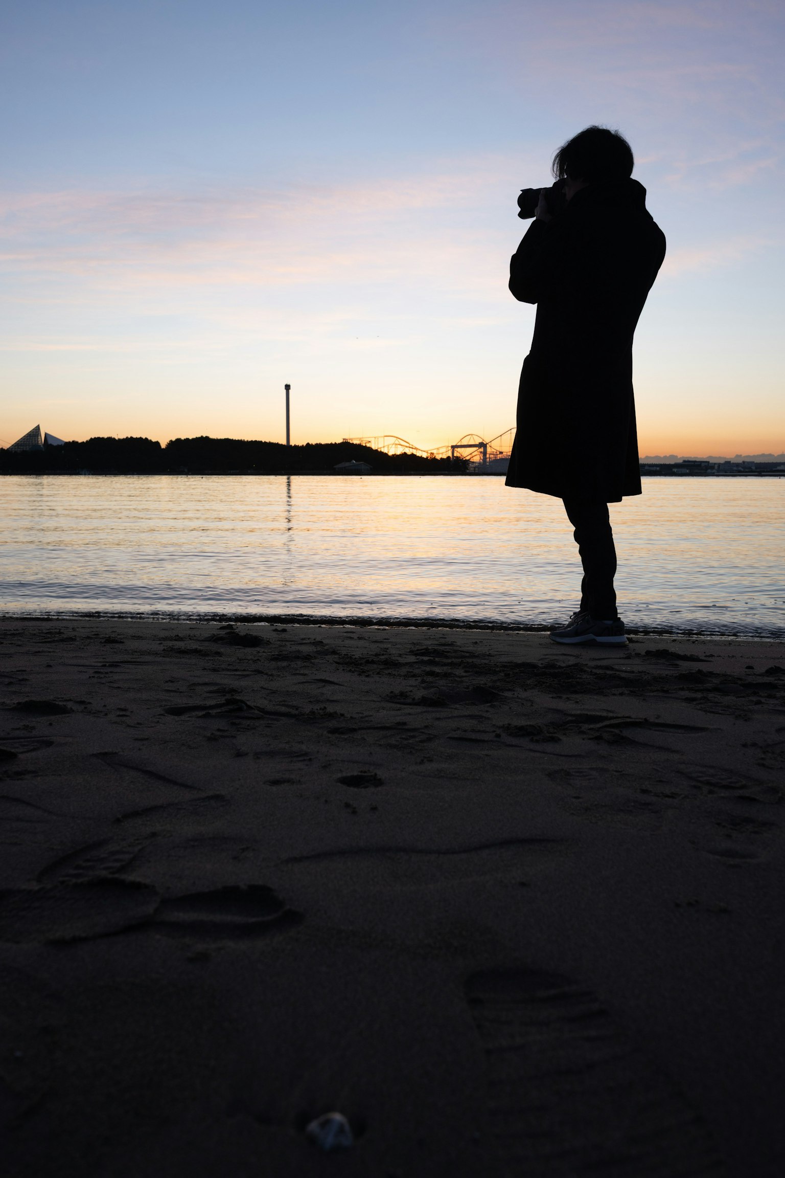 Silueta de una persona sosteniendo una cámara en la playa al atardecer