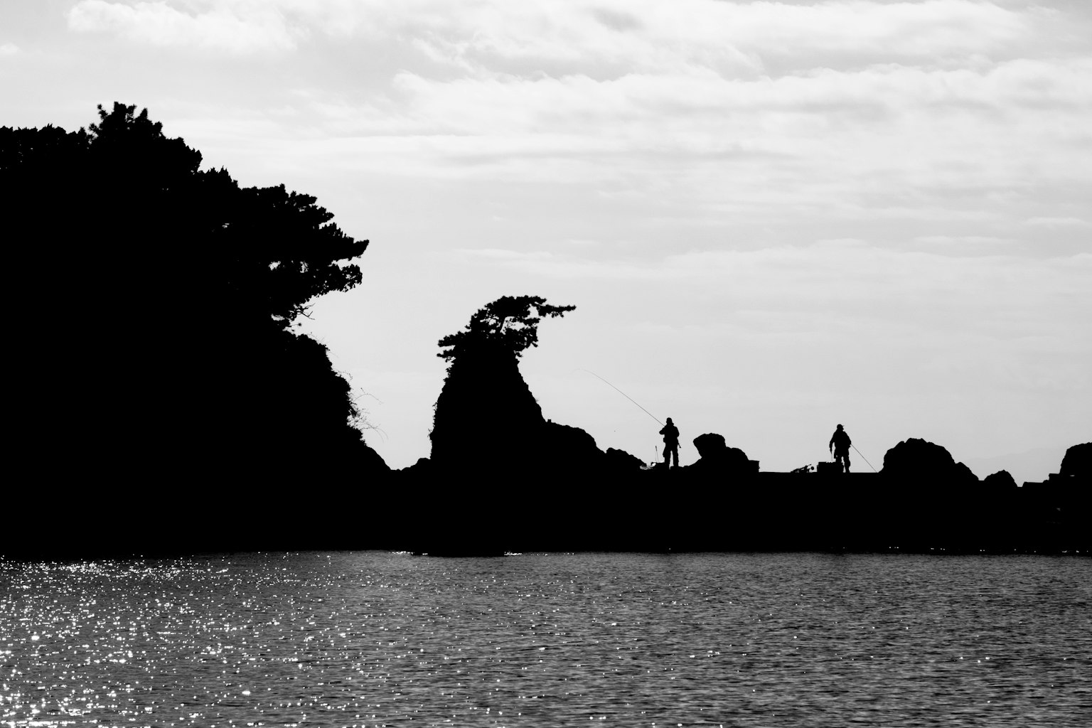 Black and white silhouette of a coastline with figures along the shore