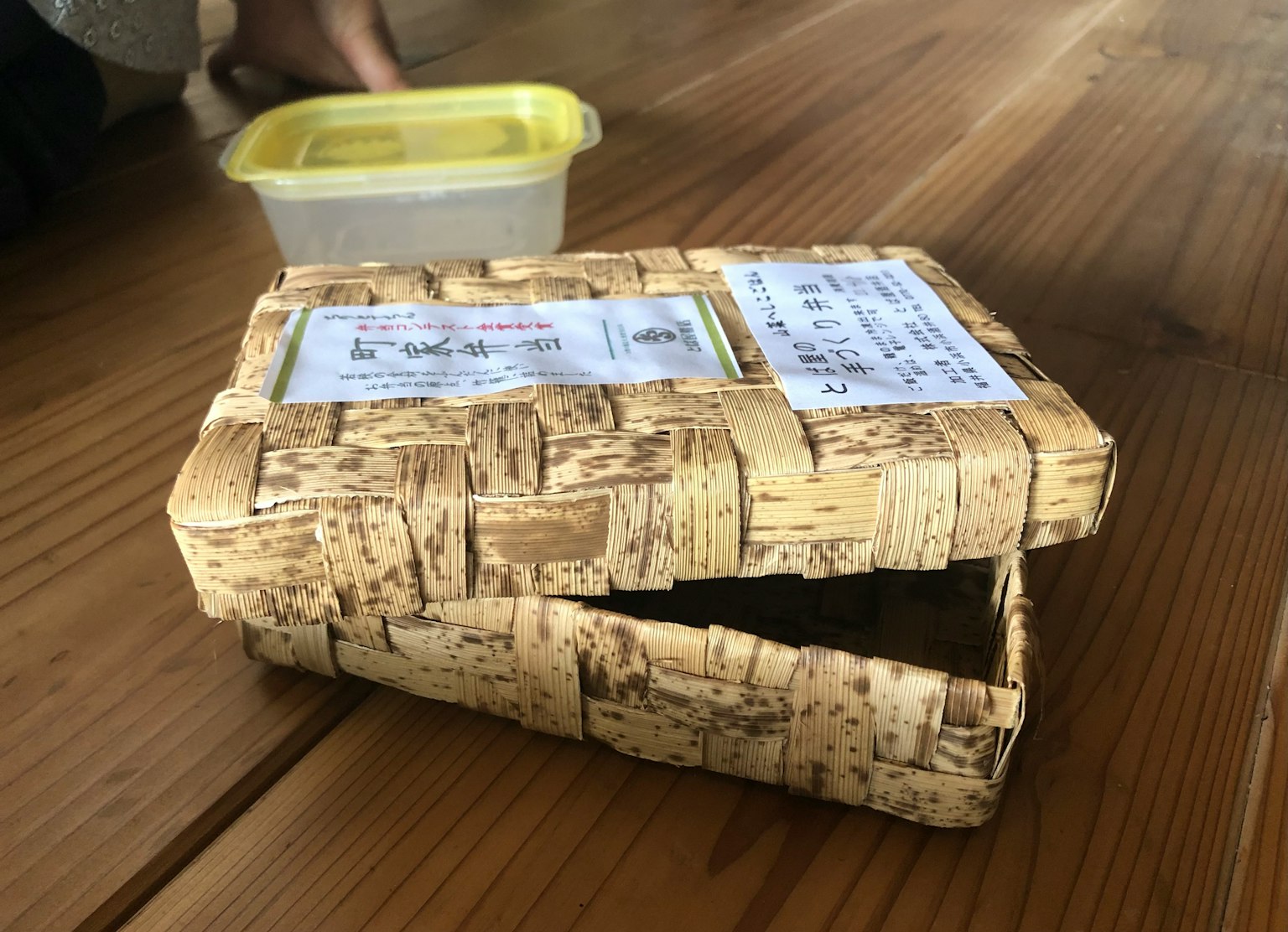 Una scatola di bambù intrecciato e un contenitore di plastica posati su un tavolo di legno