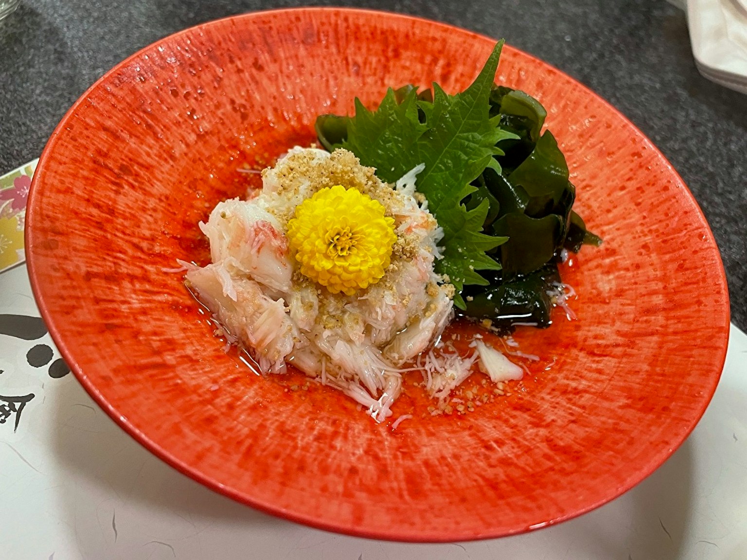 Sashimi segar disajikan di piring merah cerah dengan hiasan hijau