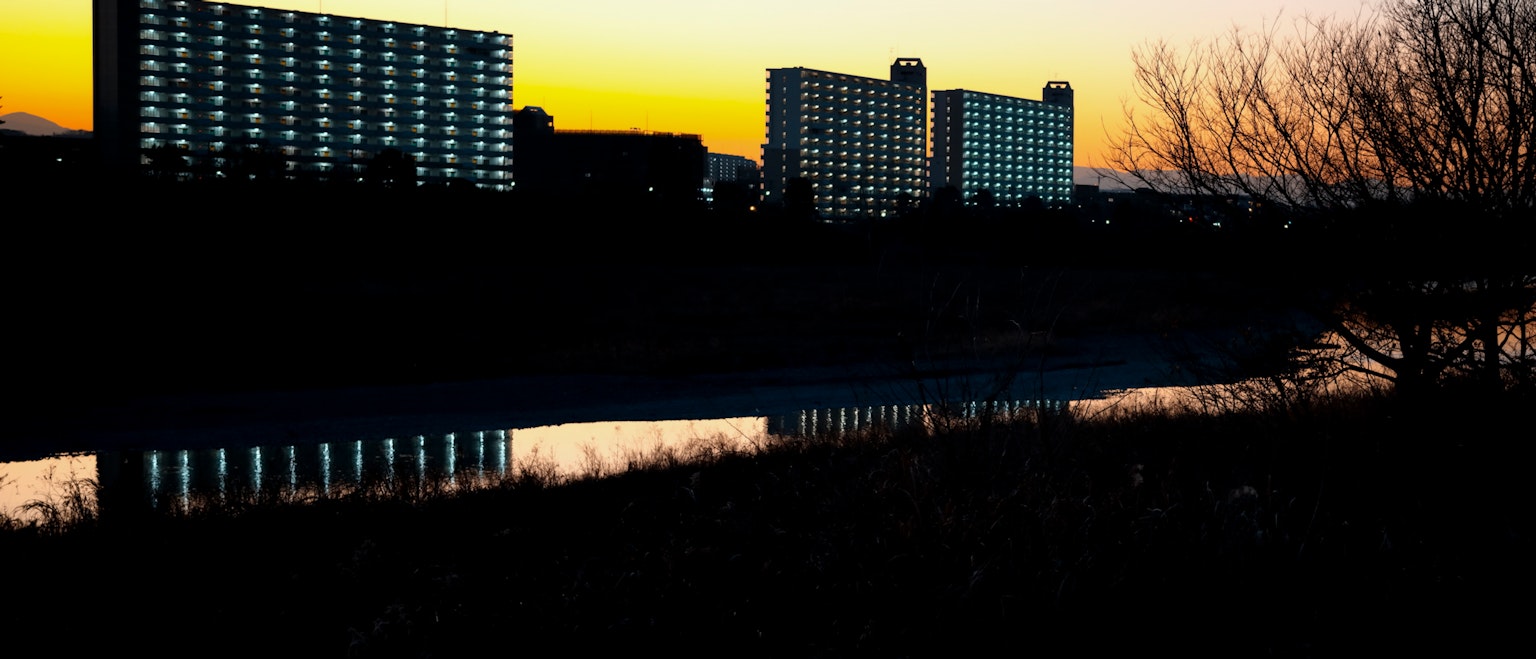 High-rise buildings silhouetted against a sunset with reflections in the river