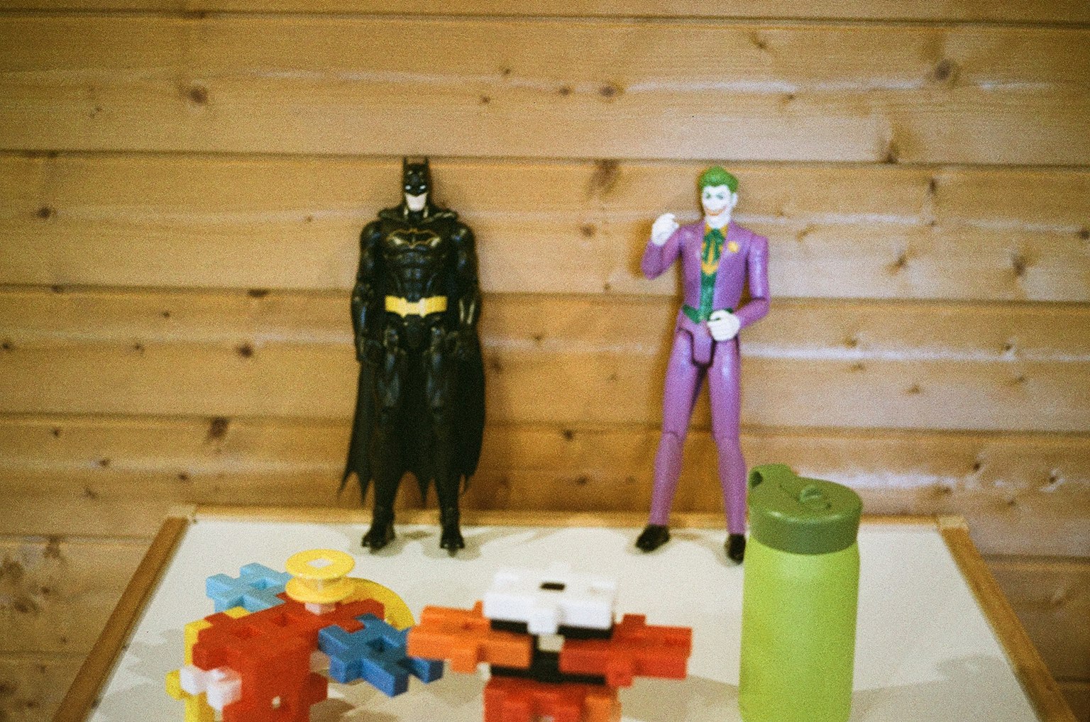 Batman and Joker action figures on a table with colorful blocks and a green container